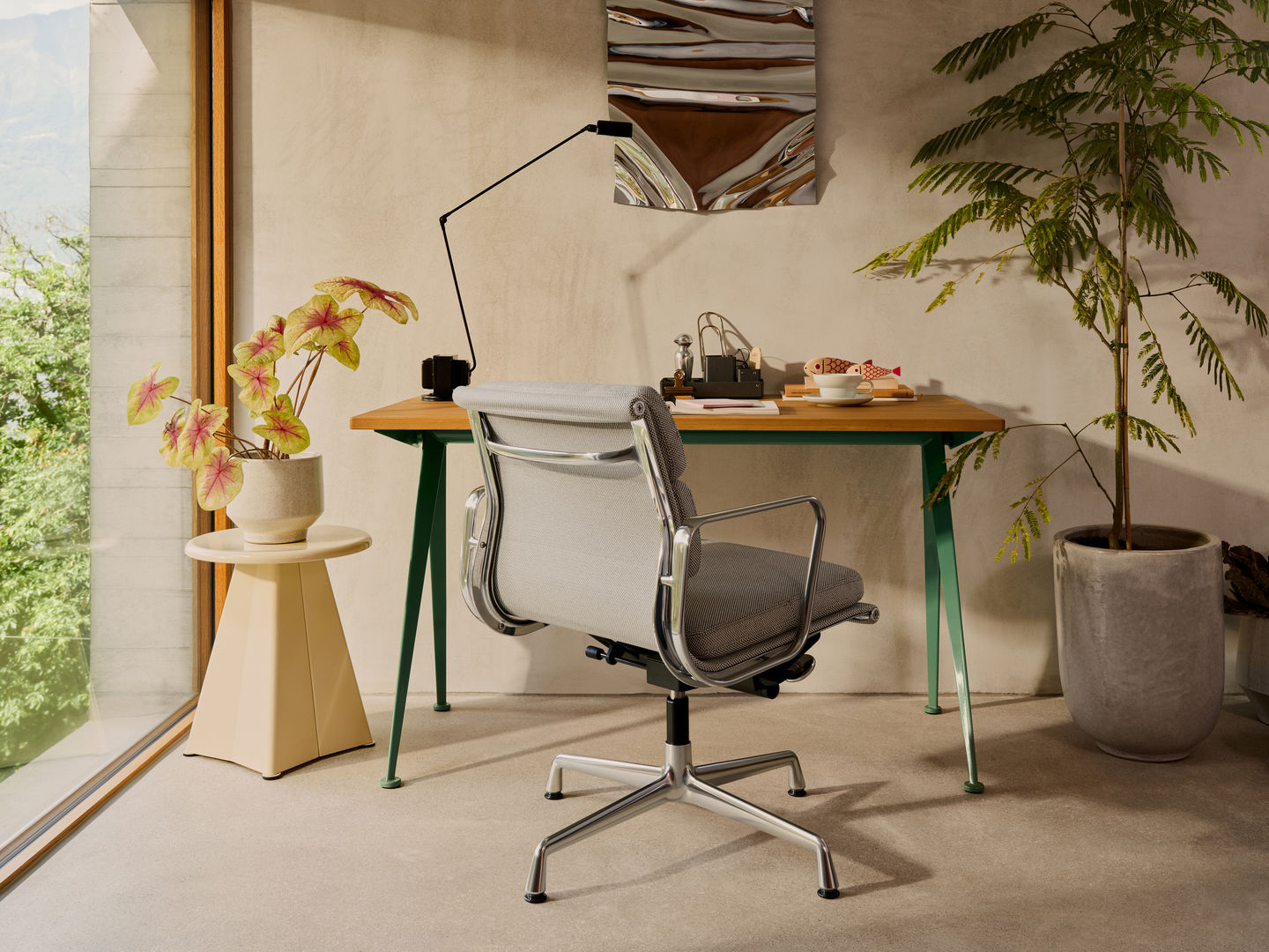 Grauer Vitra Soft Pad Chair EA 231 Bürostuhl mit Aluminiumgestell vor Schreibtisch und Pflanze.