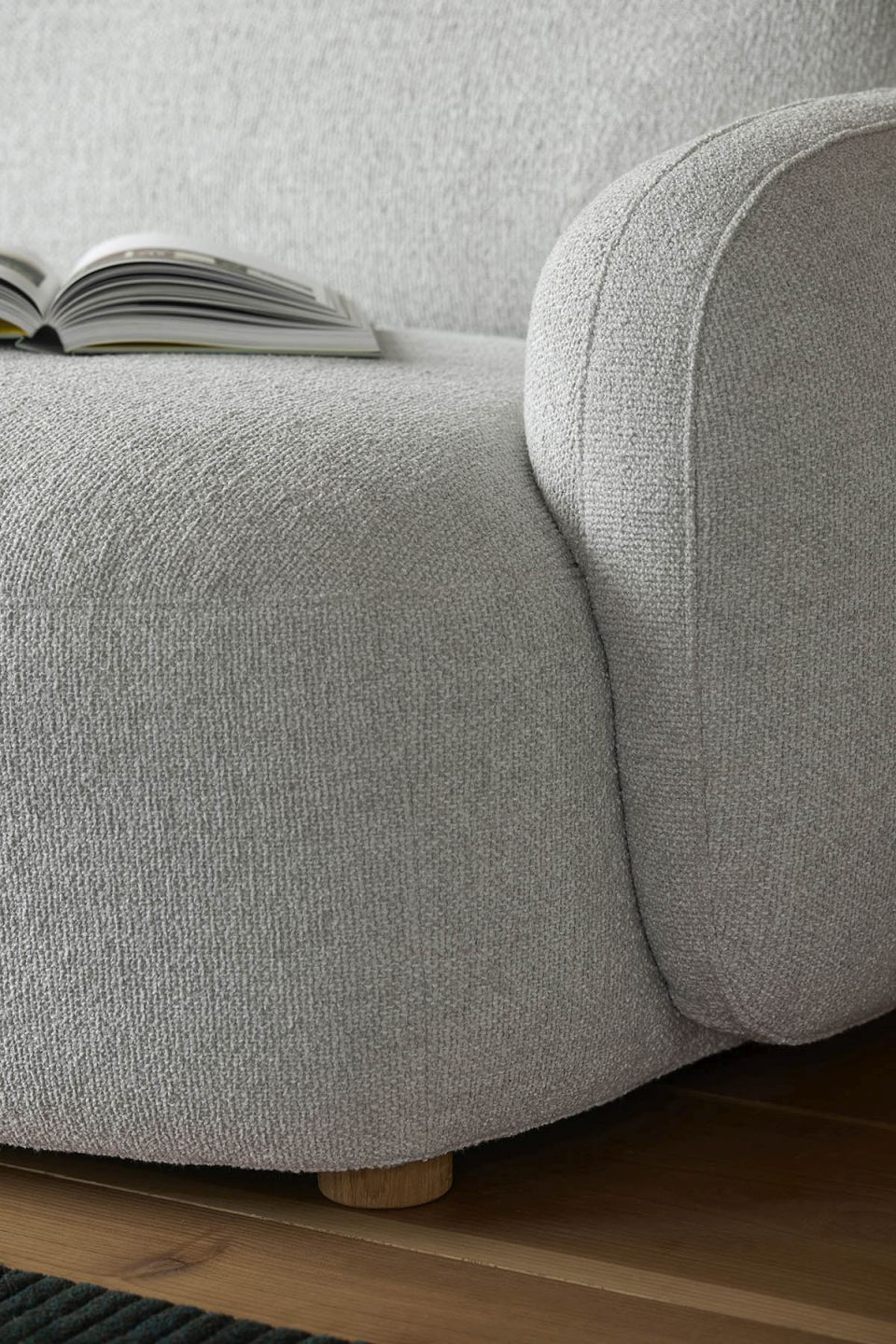 Detailaufnahme des Gem Sofas, ein modernes 3-Sitzer Sofa mit braunem Stoffbezug und Buch.