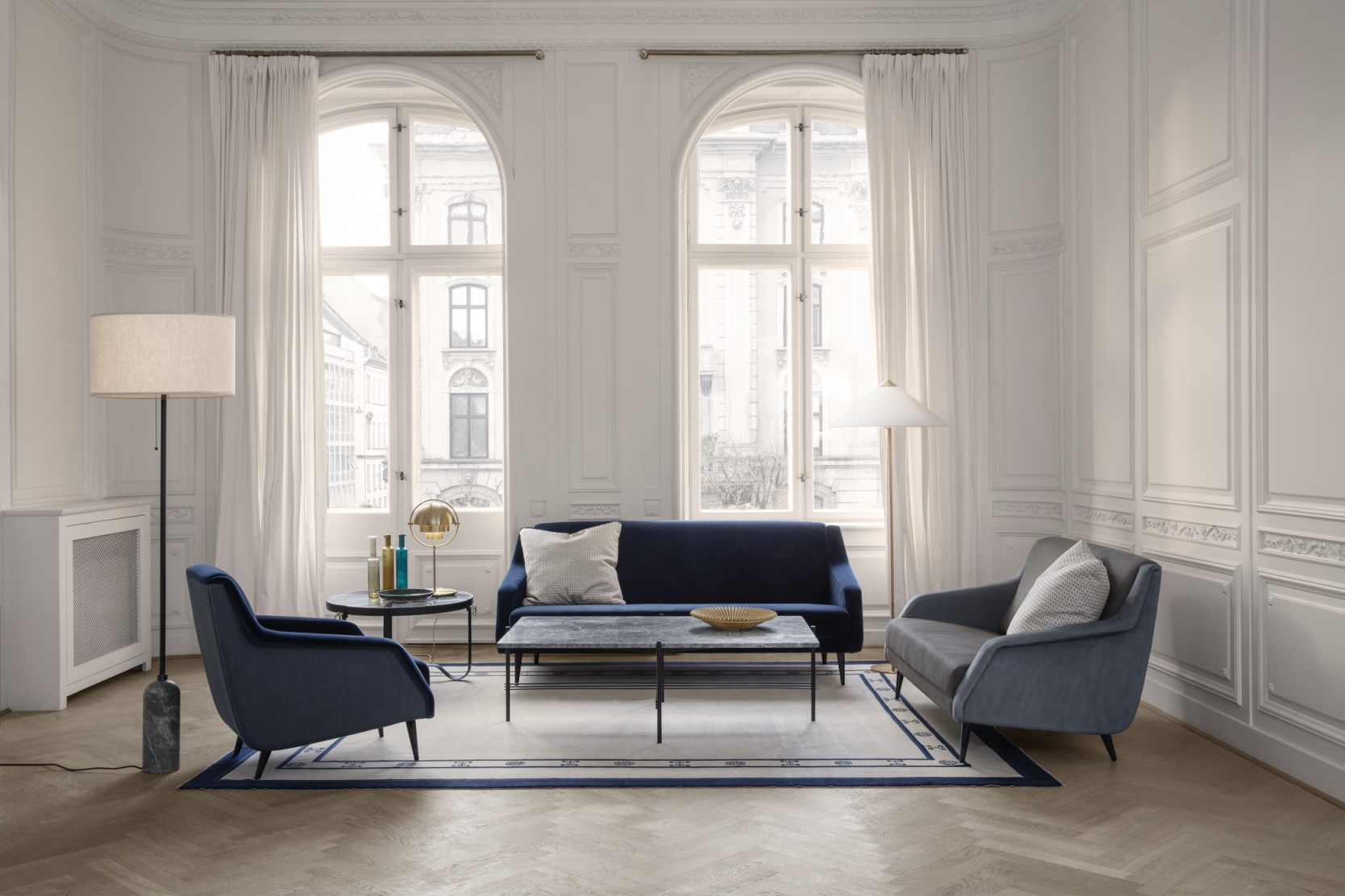 Wohnzimmer mit Gubi Adnet Couchtisch, schwarzem Leder, Sofa und Sesseln in Blau und Grau.