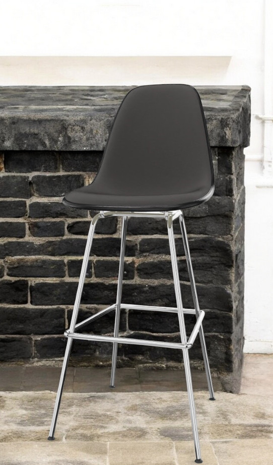 Schwarzer Eames Plastic Bar Stool Barhocker von Vitra mit Chromgestell vor einer Steinwand.