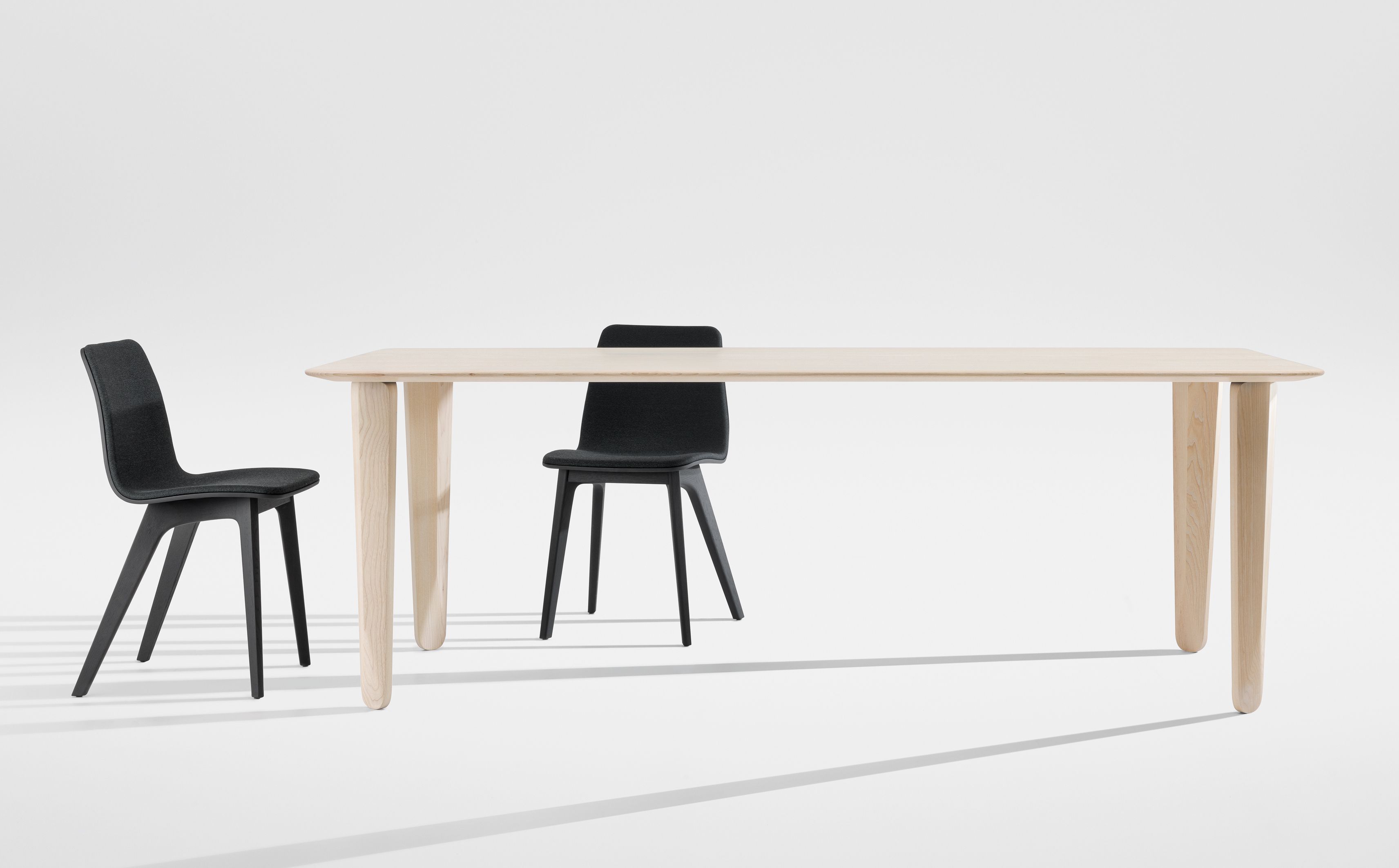 Kuyu Dine Esstisch aus hellem Holz mit zwei schwarzen Stühlen vor weißem Hintergrund.