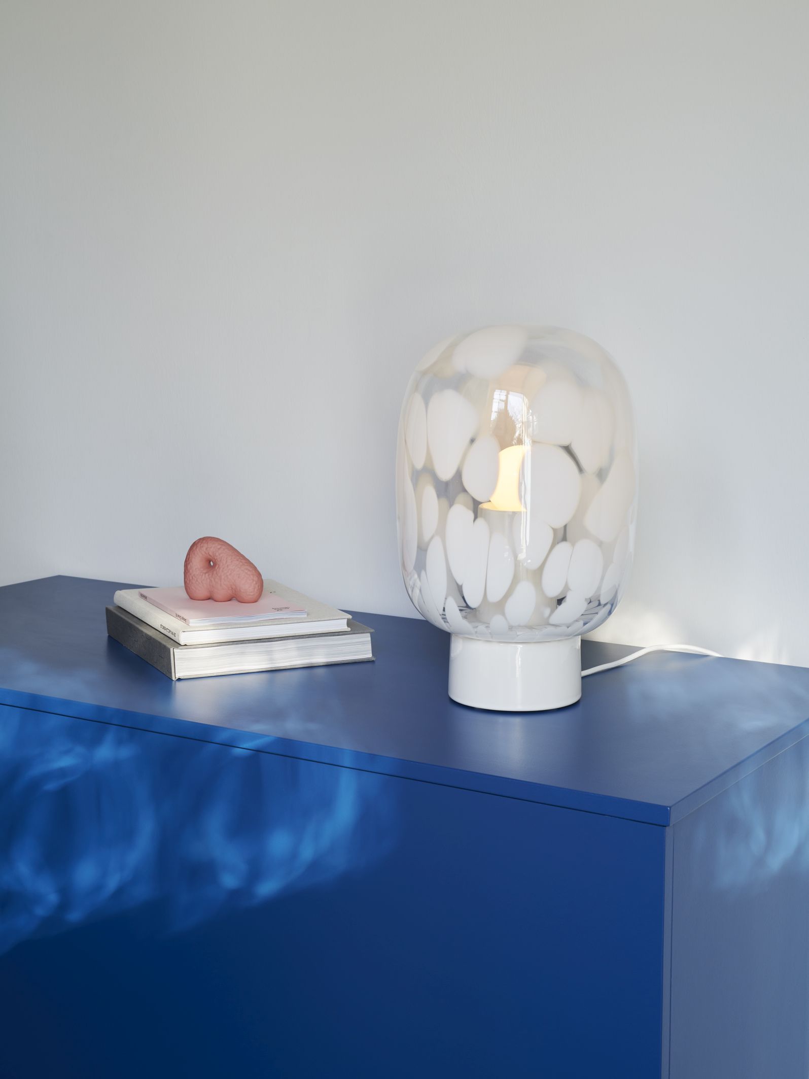 Weiße Flakes Tischleuchte mit Kristallglas auf blauem Schrank, moderne Wohnraumbeleuchtung.