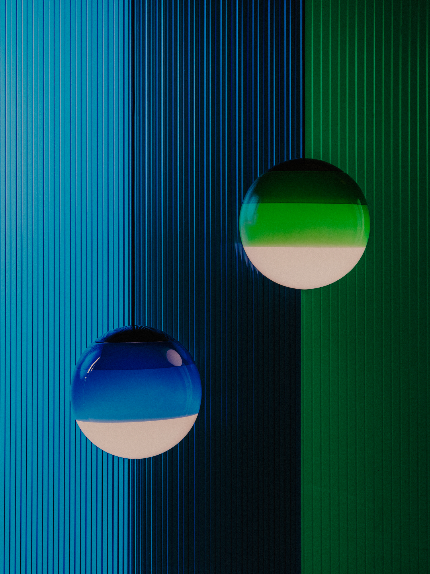 Dipping Light Pendelleuchten in Grün und Blau vor farbigen, geriffelten Hintergründen.