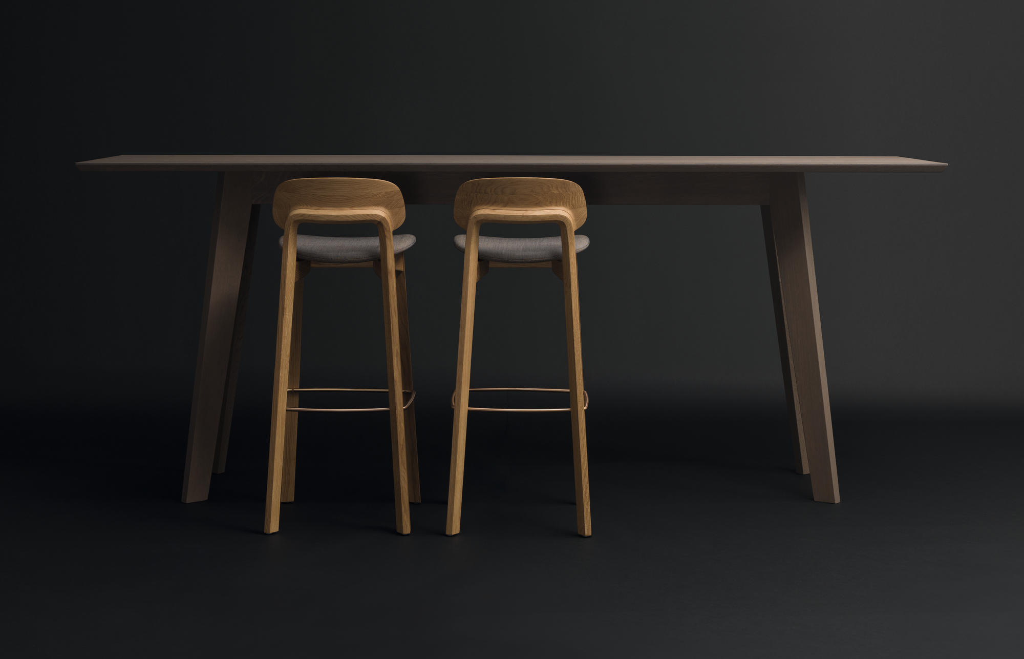 Zwei Nonoto Barhocker aus Nussbaum mit grauen Sitzen an einem Bartisch.