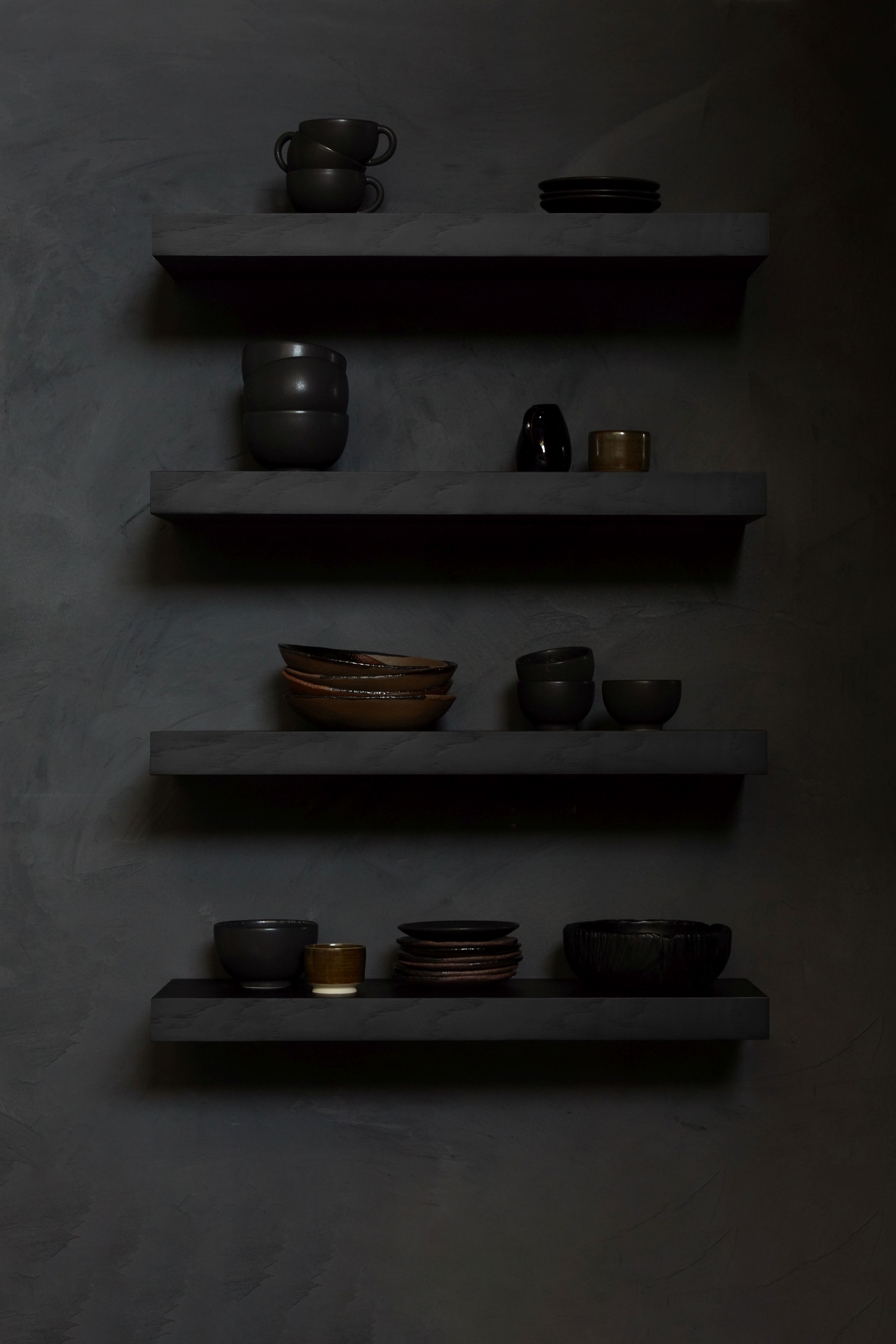 Schwarzes Ethnicraft Wandregal aus Eiche mit lackierter Oberfläche, dekoriert mit Geschirr und Vasen vor dunkler Wand.