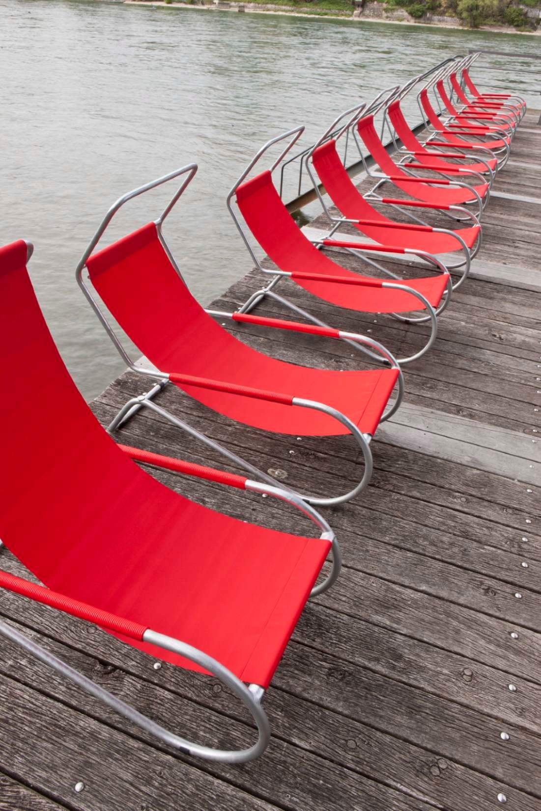 Reihe roter Lido Liegen auf Holzsteg am Wasser. Moderne Gartenmöbel für Entspannung.