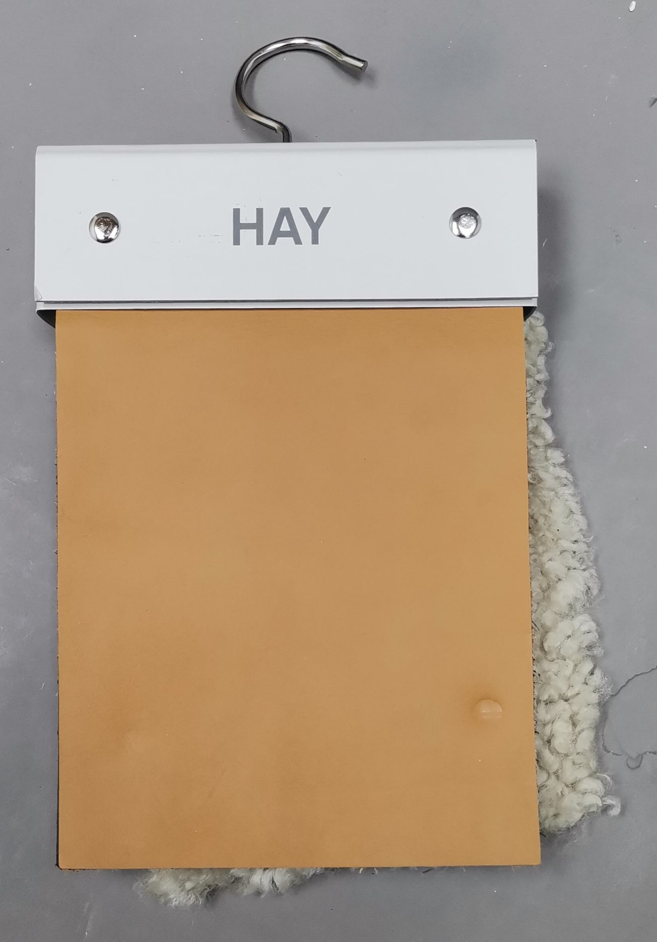 Muster von Hay: Leder- und Canvas-Stoffprobe in Braun und Weiß mit Metallaufhängung.