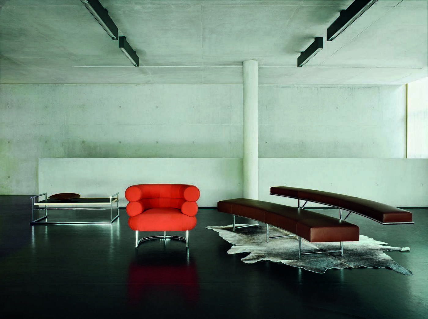 Menton Tisch von ClassiCon, orangefarbener Sessel und braune Bänke mit Chromgestell in modernem Raum.