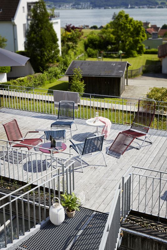 Gartenmöbel Set aus Stühlen und Tischen auf einer Holzterrasse mit Blick auf den See.