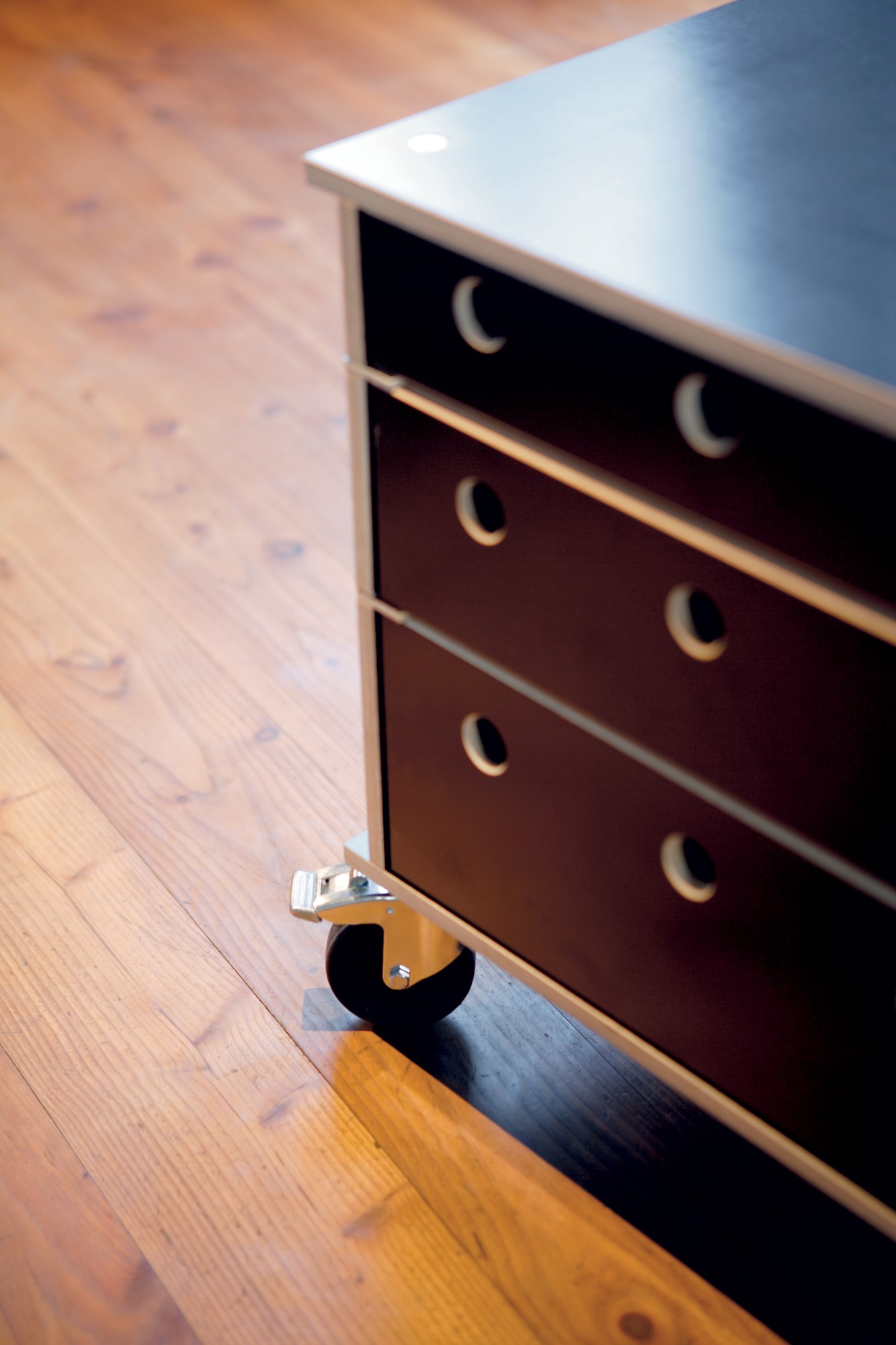 Detailaufnahme: Moormann Lader Schubkastensystem mit Rollen auf Holzboden, braune Schubladen mit runden Griffen.