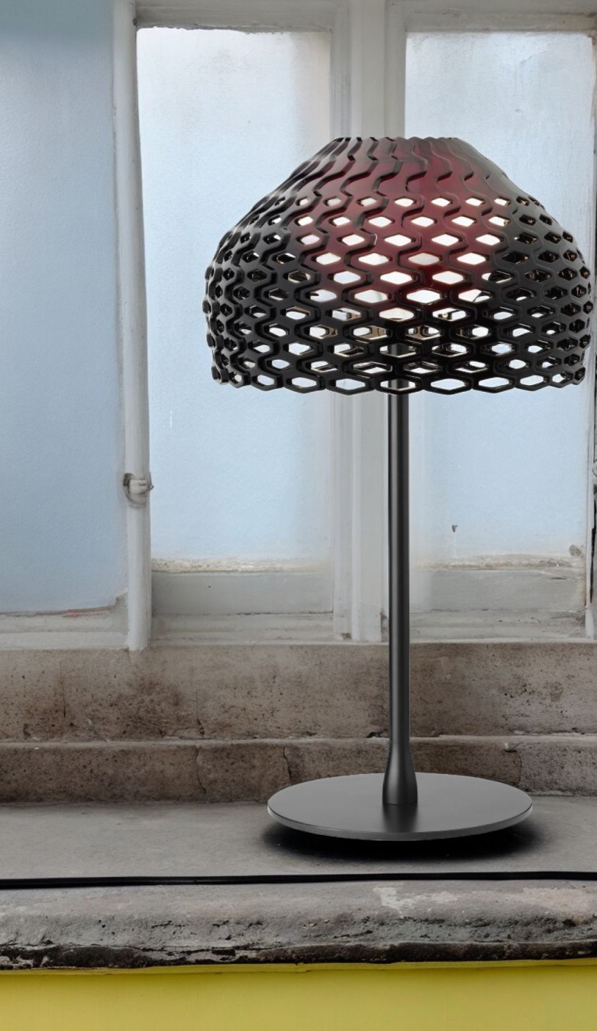 Schwarze Tatou T1 Tischleuchte von Flos mit filigranem Lampenschirm aus Kunststoff vor einem Fenster.