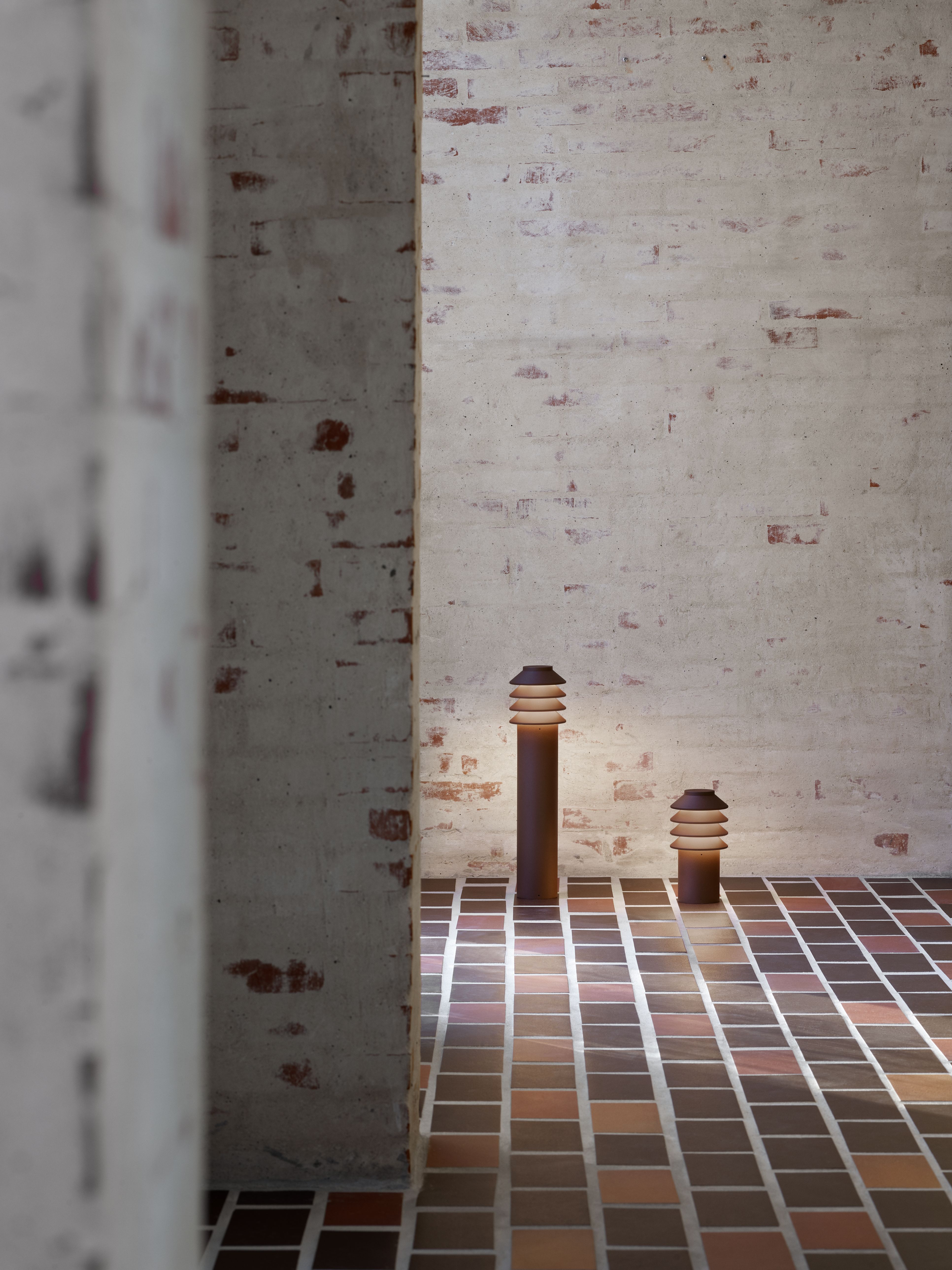 Zwei Bysted Garten Pollerleuchten von Louis Poulsen beleuchten einen gefliesten Außenbereich.