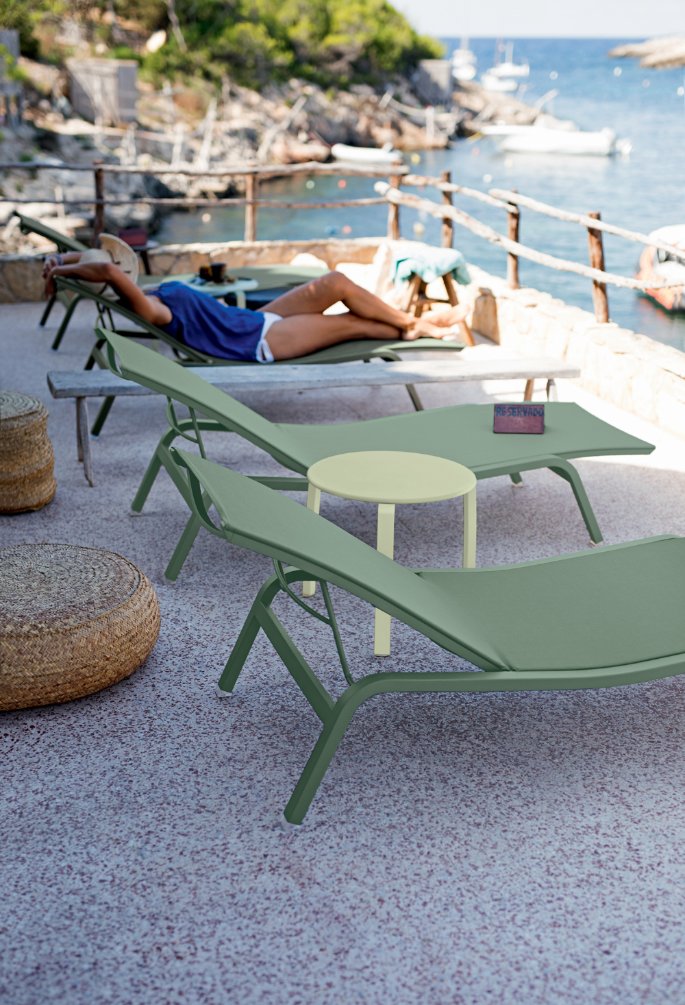 Alizé Outdoor Tisch von Fermob neben grünen Liegen am Meer. Outdoor Möbel für Garten und Terrasse.