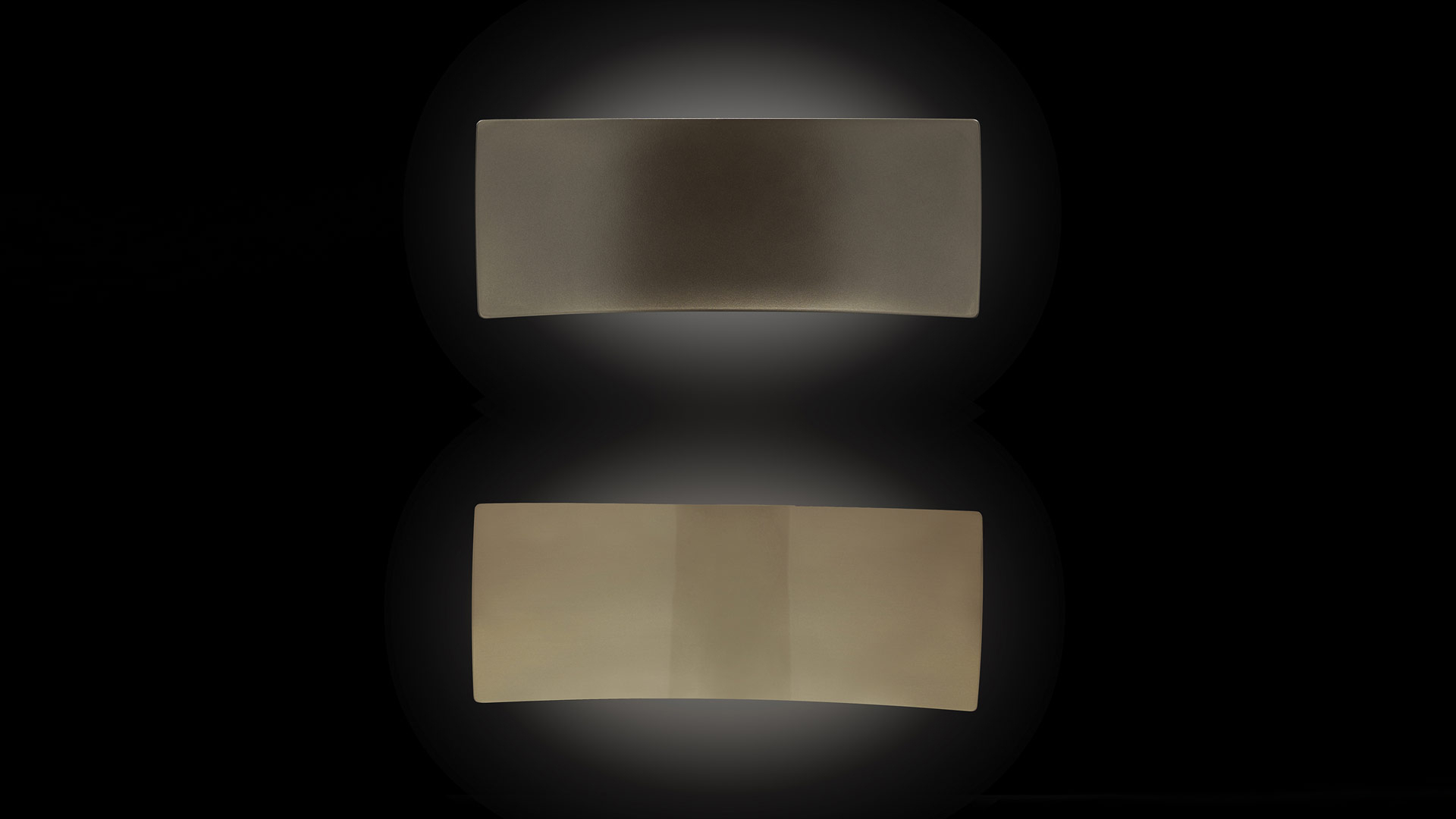 Oluce Lens Wandleuchte: Zwei rechteckige, goldfarbene Wandlampen mit indirektem Licht auf schwarzem Hintergrund.