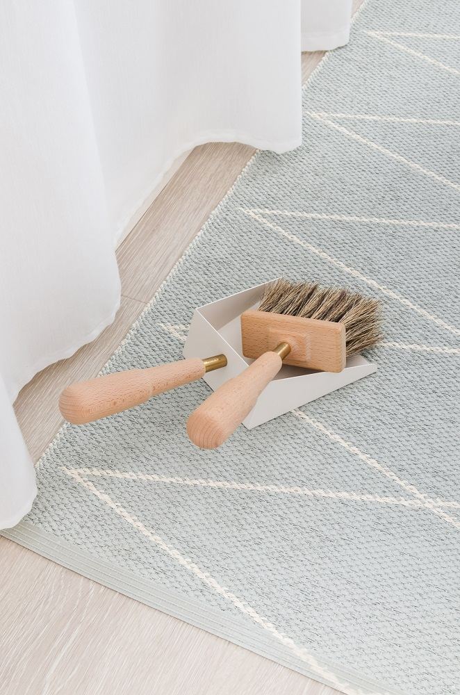 Detailaufnahme: Pappelina Max Kunststoffteppich in Schlamm mit geometrischem Muster und Reinigungsbürste.