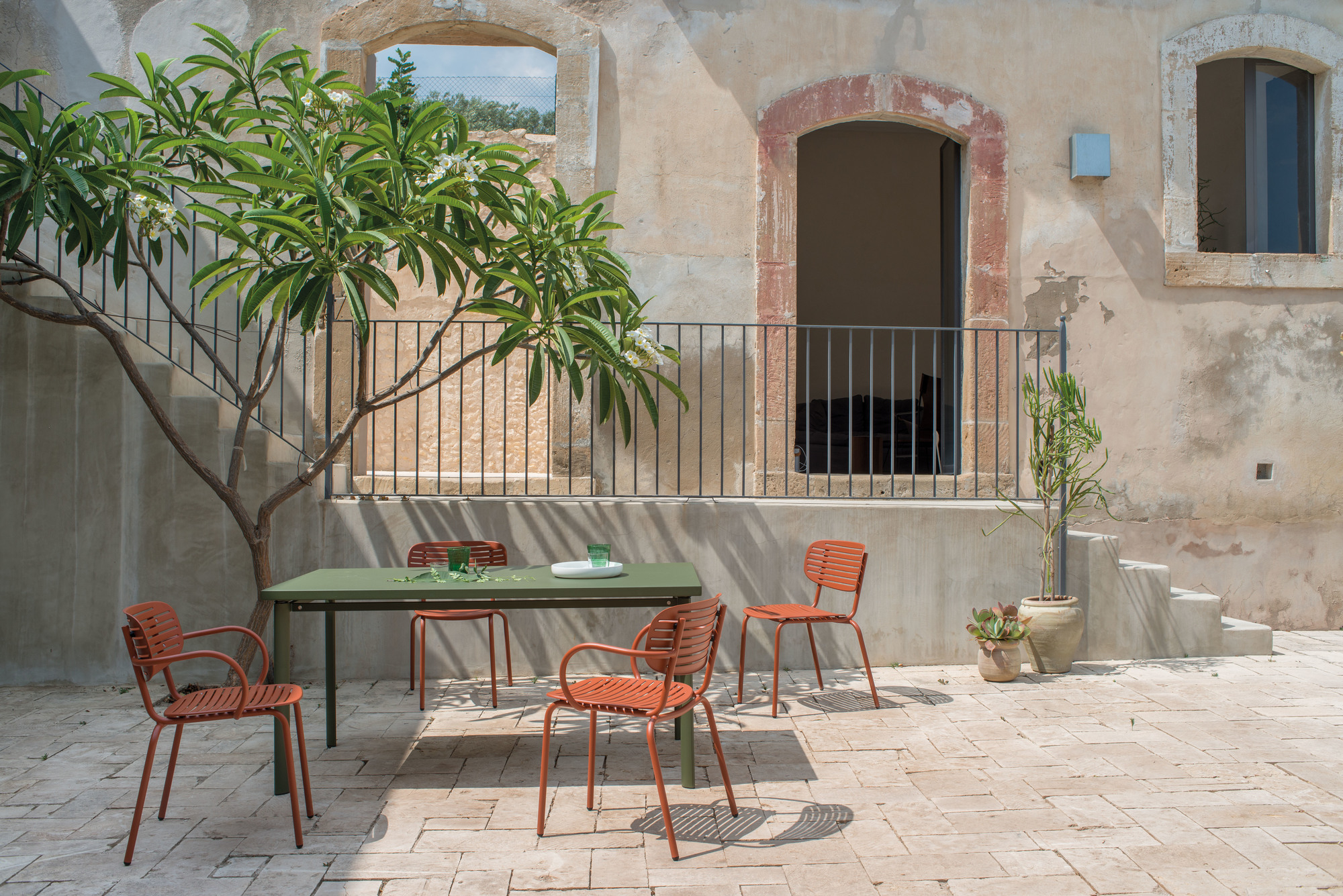 Emu Mom Armlehnenstuhl in Terrakotta und grüner Tisch im mediterranen Außenbereich. Gartenmöbel für Terrasse.