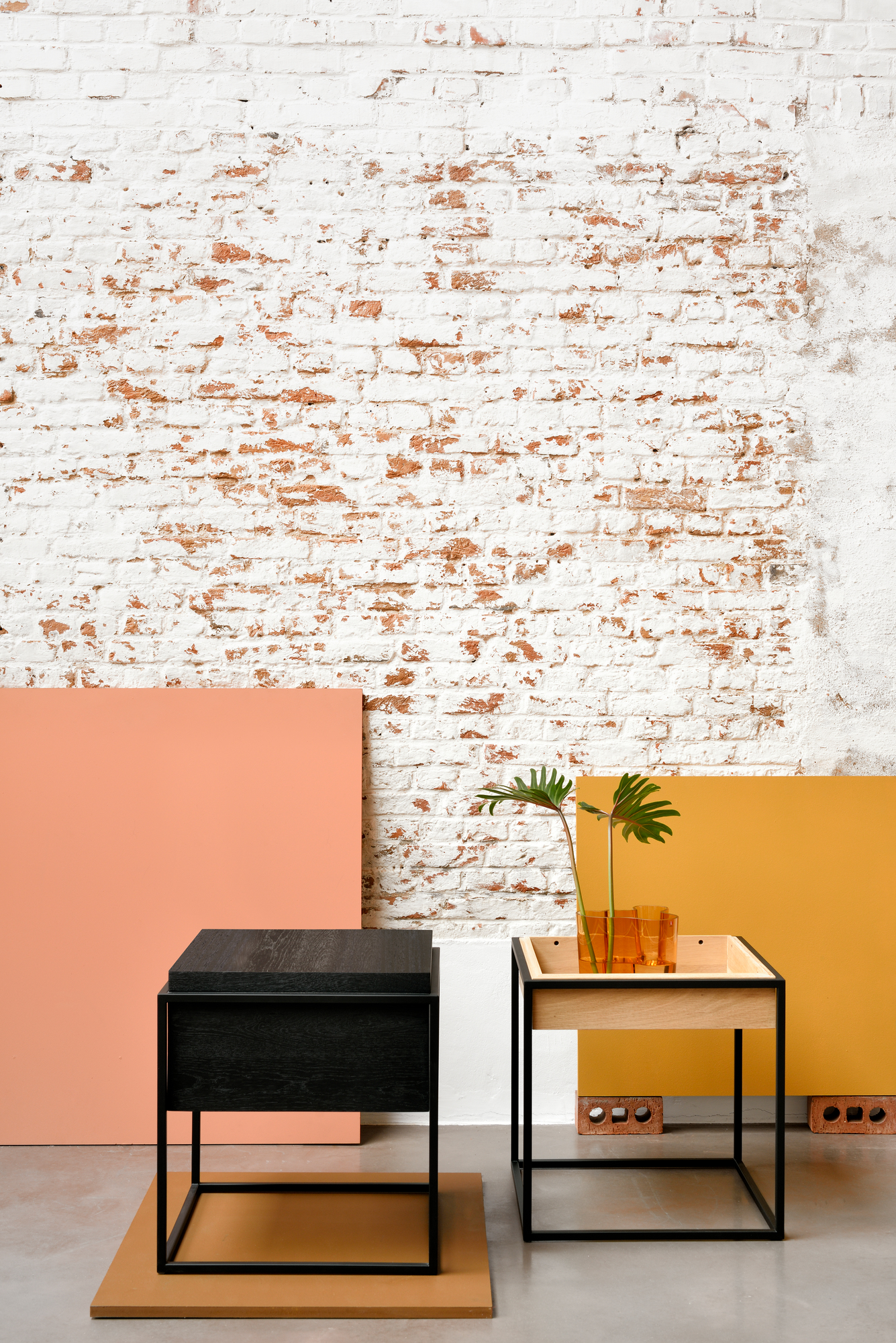 Schwarzer Ethnicraft Monolit Beistelltisch aus Eiche neben einem hellen Eichenholz Beistelltisch mit Pflanze.