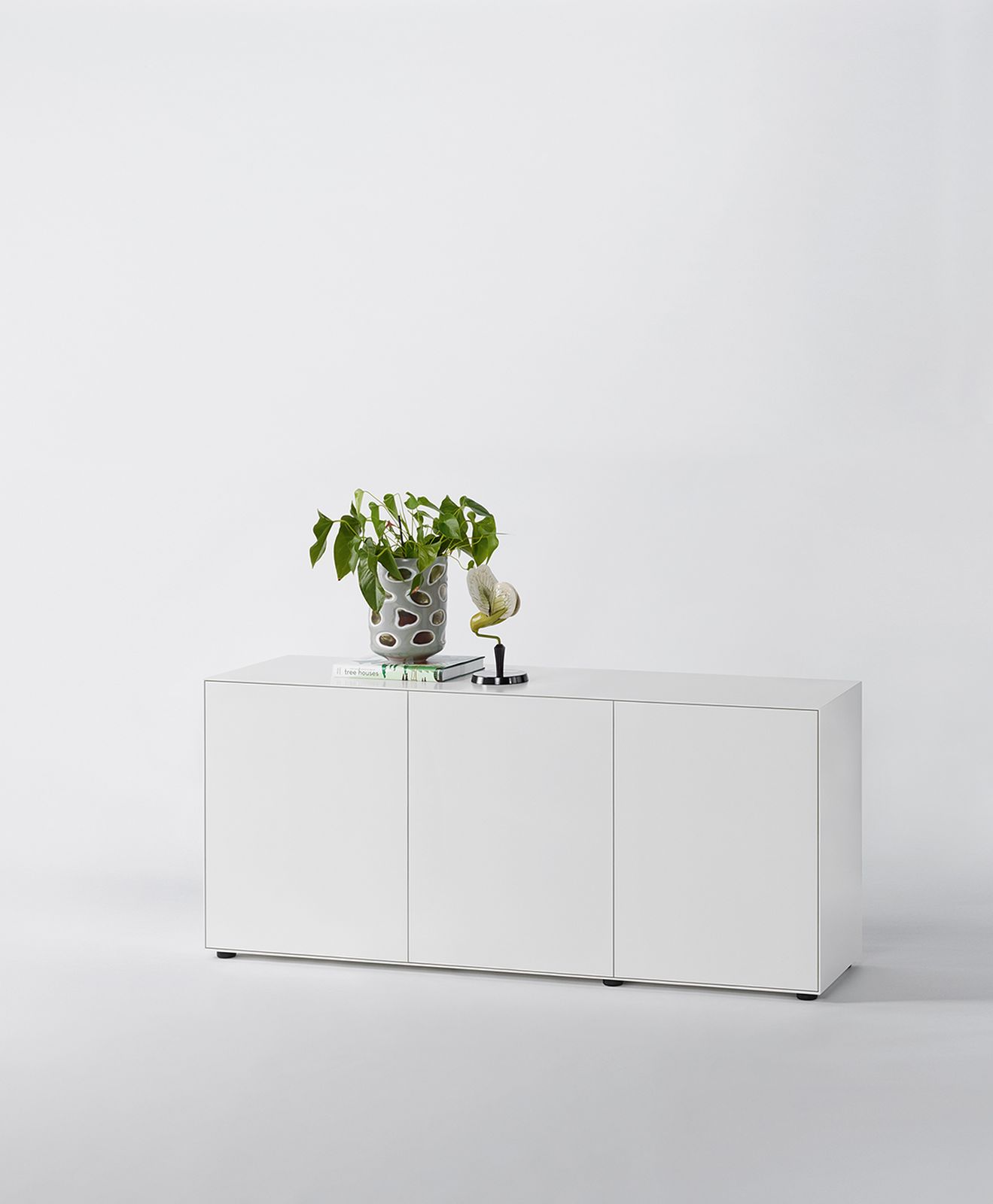 Weißes Nex Pur Box Board mit drei Türen, dekoriert mit Pflanze und Deko-Objekt.