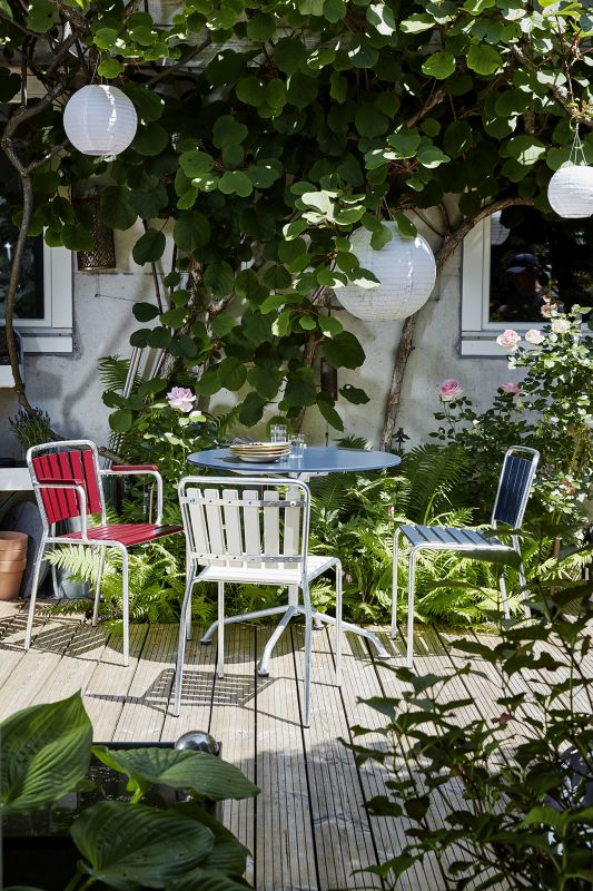 Gartenszene mit blauem Gartentisch und bunten Gartenstühlen aus Metall auf einer Holzterrasse.