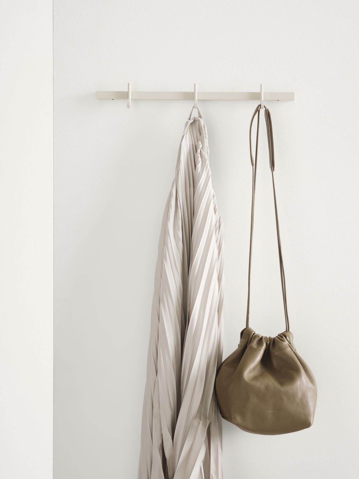 Relief Hakenleiste Esche von String Furniture mit Jacke und Tasche an weißer Wand.