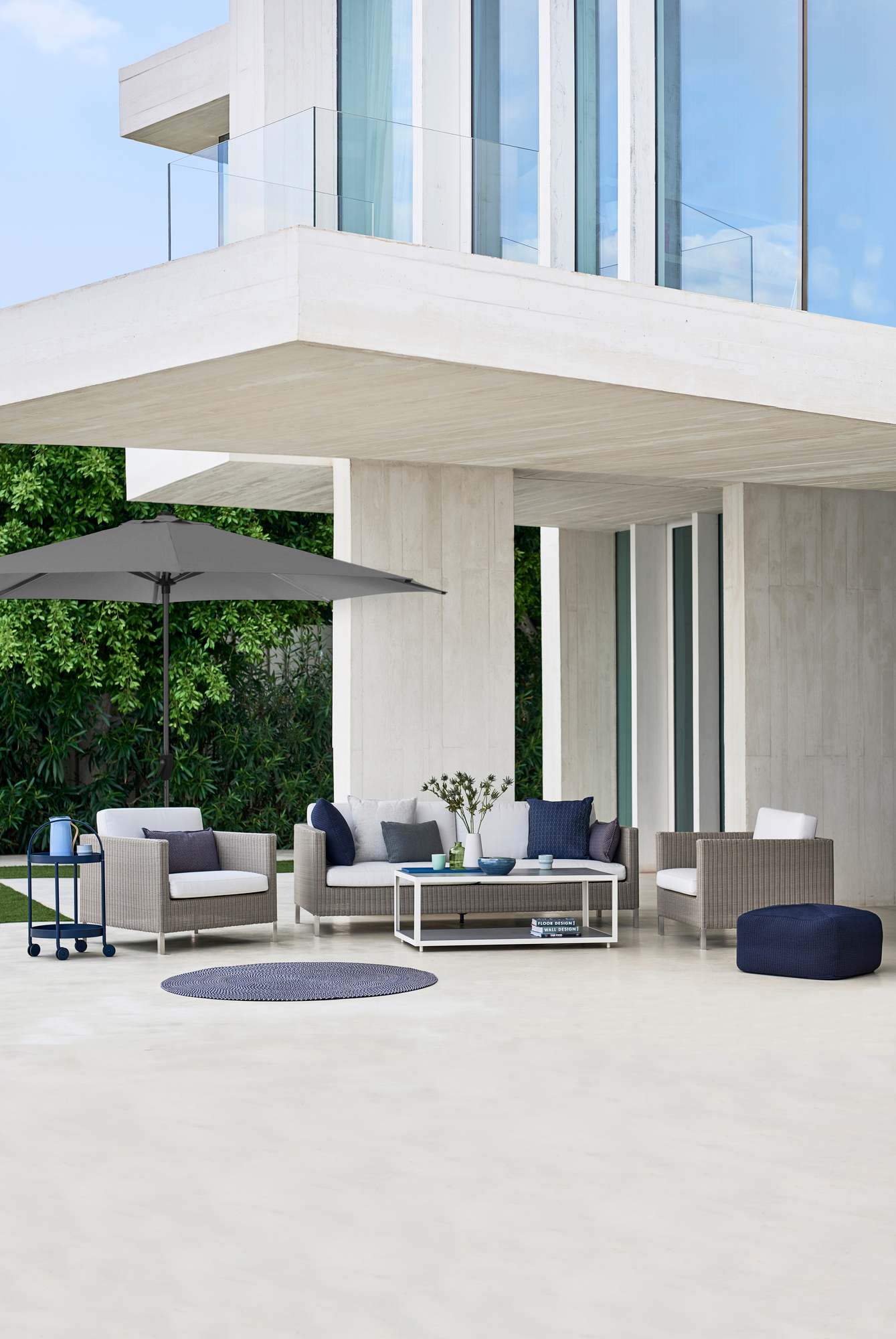 Grauer Sonnenschirm mit Cane-Line Sonnenschirmfuß im modernen Outdoor-Lounge-Bereich. Keywords: Sonnenschutz, Gartenmöbel, Design.