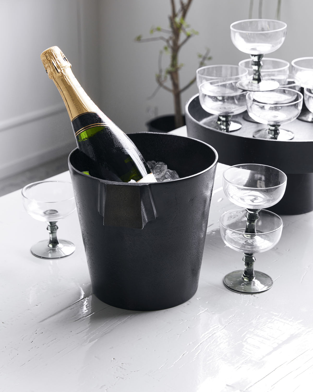 Schwarzer Buck Weinkühler von House Doctor mit Champagnerflasche und Eiswürfeln, daneben Cocktailgläser.