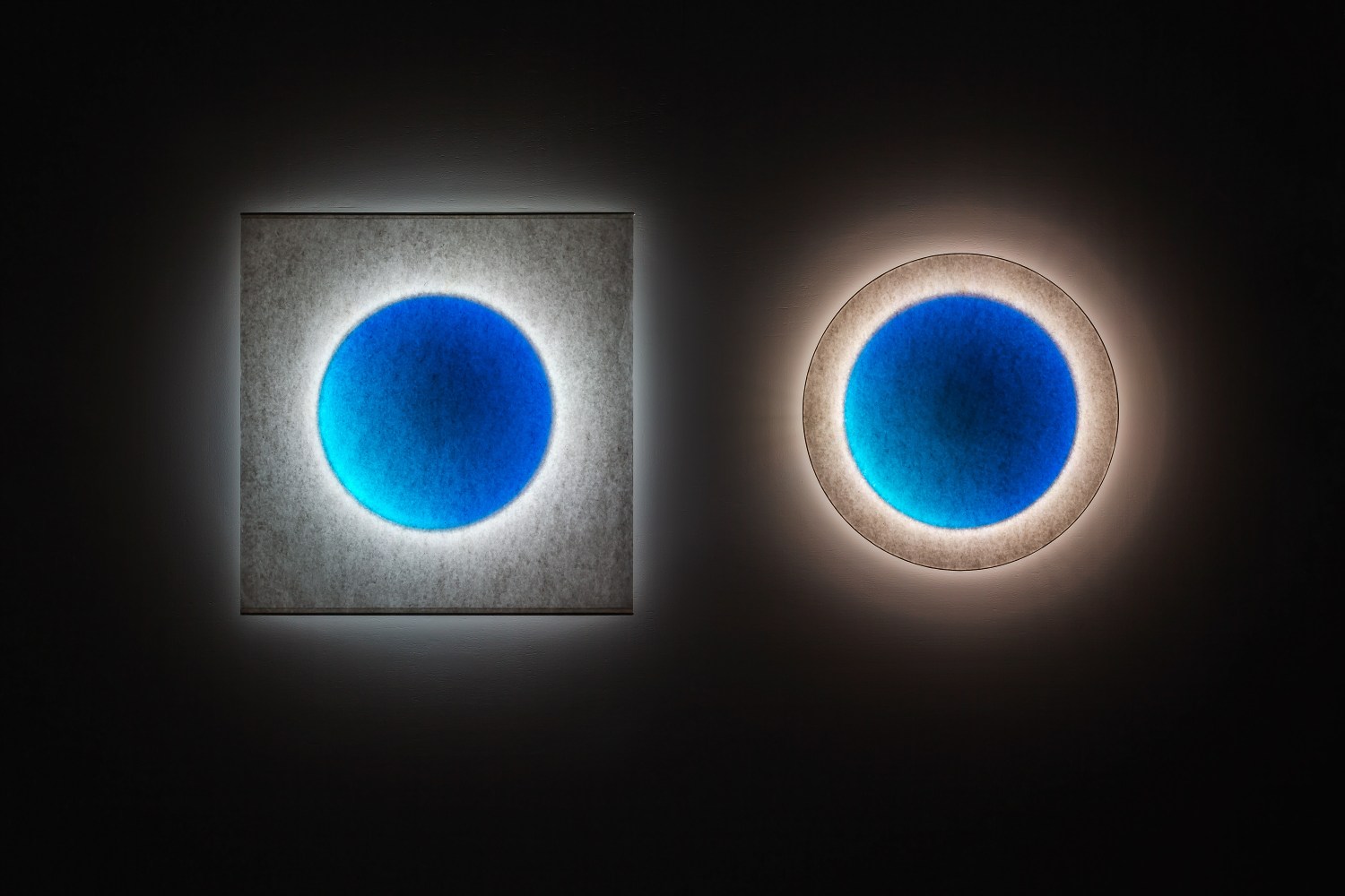 Zwei Moodmoon Wandleuchten: Rund und quadratisch, blaues Zentrum, indirekte Beleuchtung.