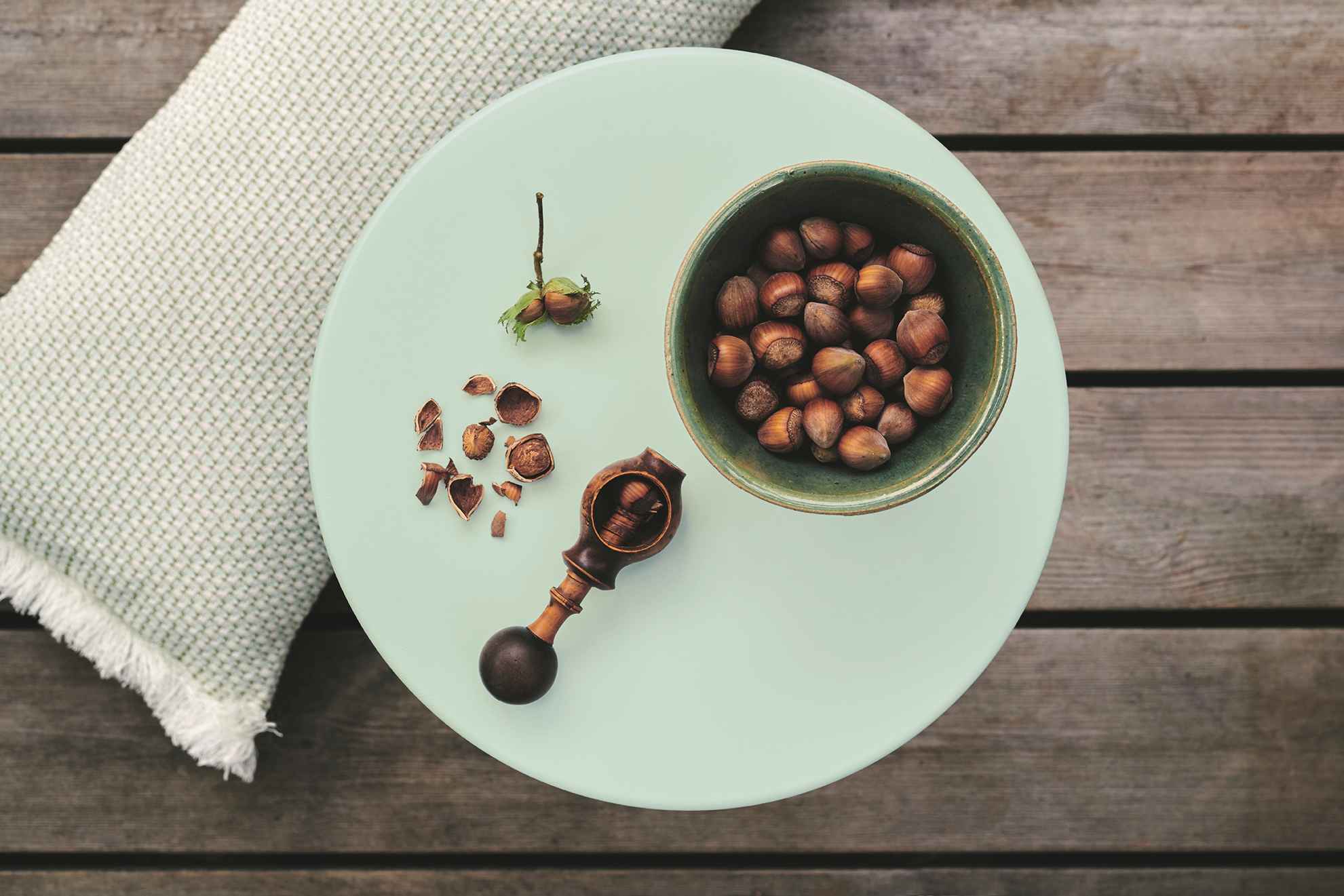 Cocotte Beistelltisch von Fermob in Hellgrün mit Nüssen, Nussknacker und Kissen auf Holzterrasse.