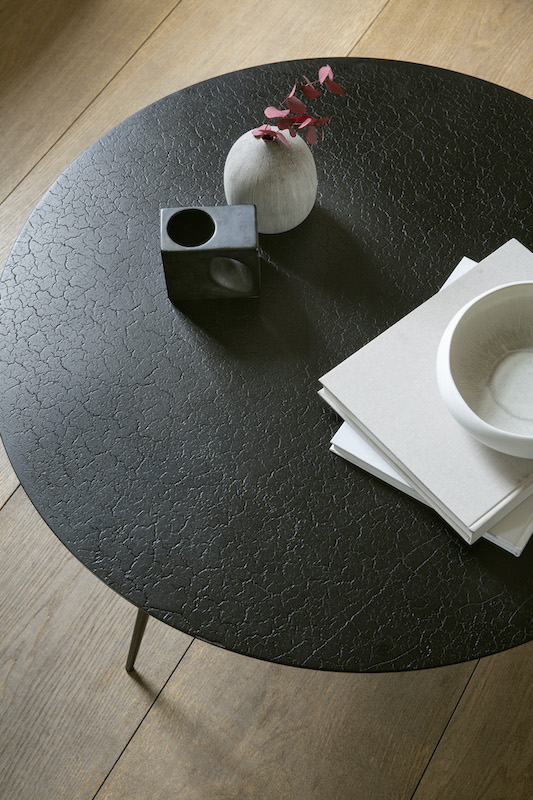 Runder, schwarzer Couchtisch mit Lava-Textur (Ethnicraft Luna) und Deko-Elementen auf Holzboden.