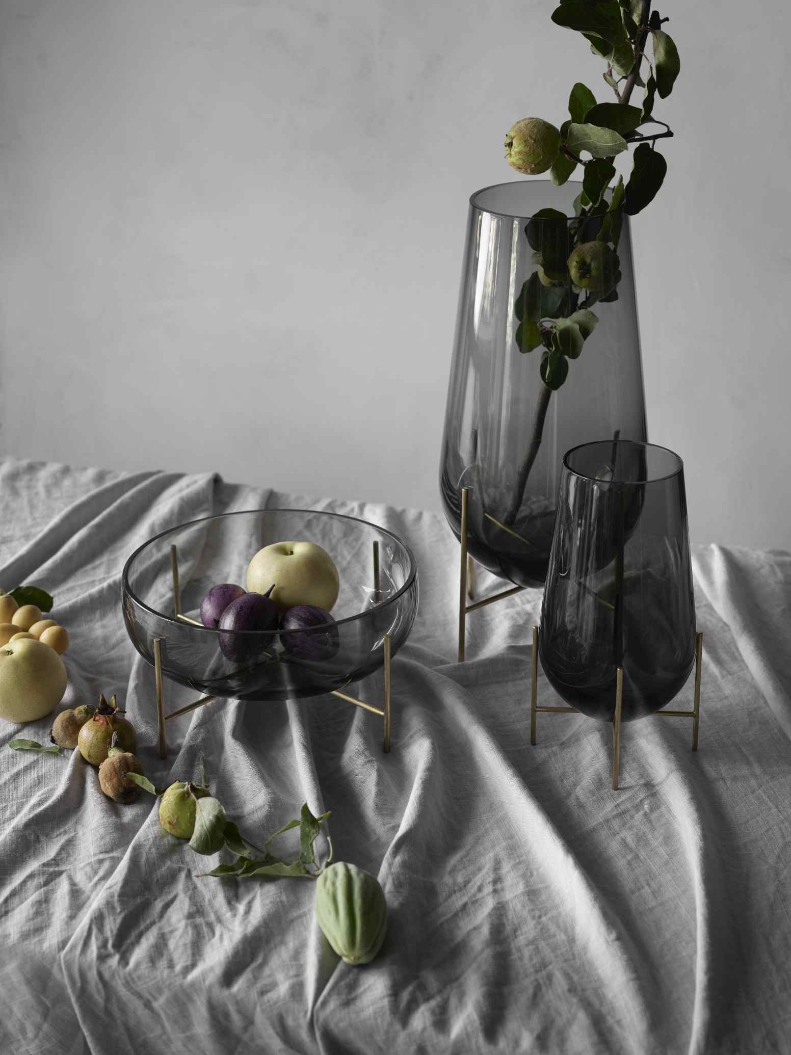 Échasse Bowl Schale auf Tisch mit Obst und Vasen. Dekorative Glasschale mit filigranem Metallgestell.