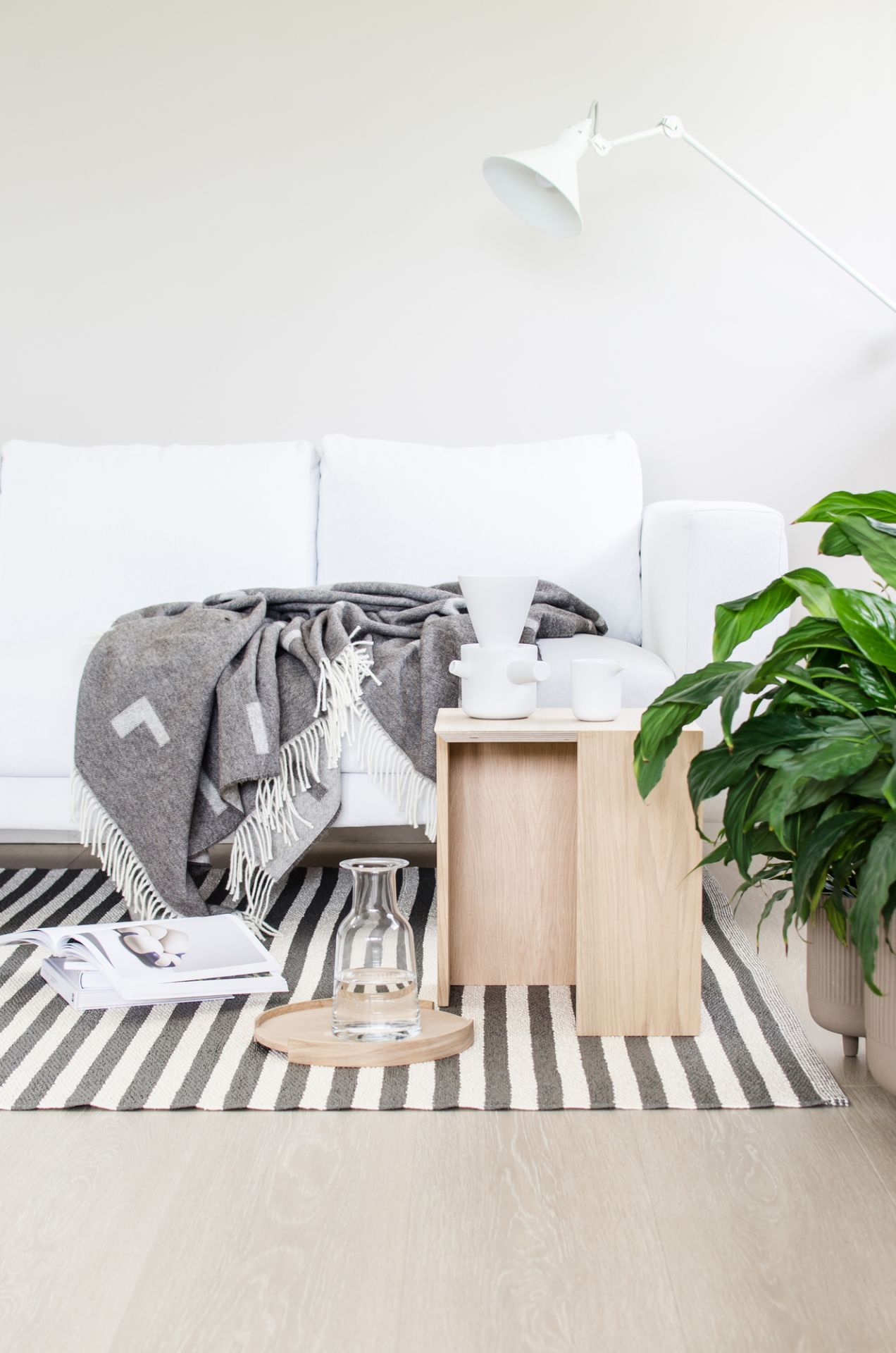 Wohnzimmer mit weißem Sofa, grauer Wolldecke, Holztisch und gestreiftem Teppich für gemütliche Atmosphäre.