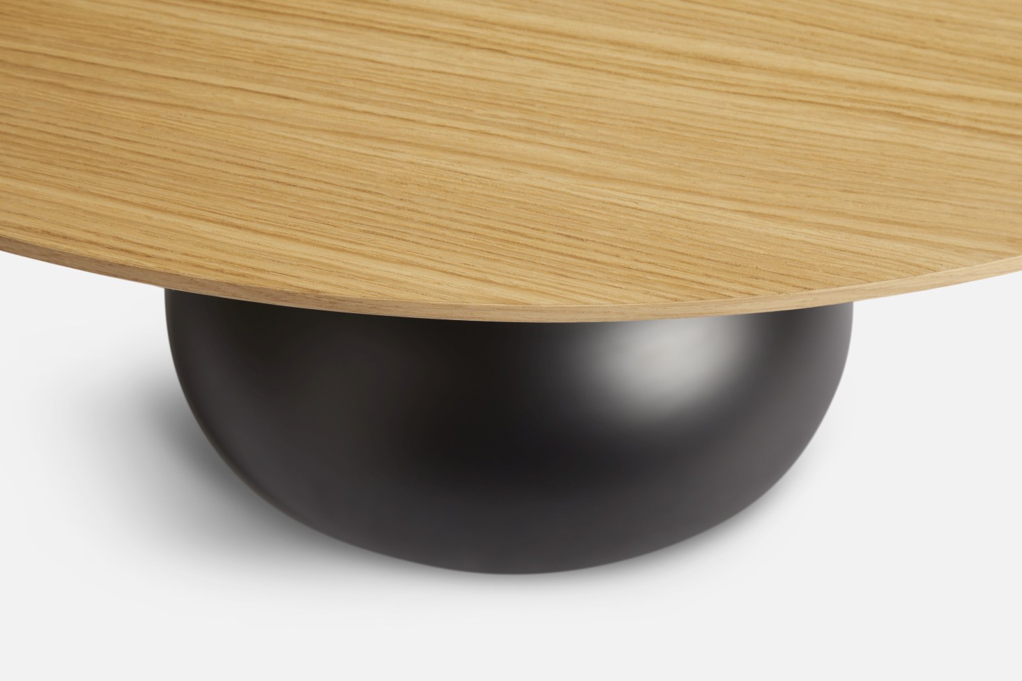 Detailaufnahme: Woud Esstisch mit runder Tischplatte aus hellem Holz und schwarzem, kugelförmigem Fuß.