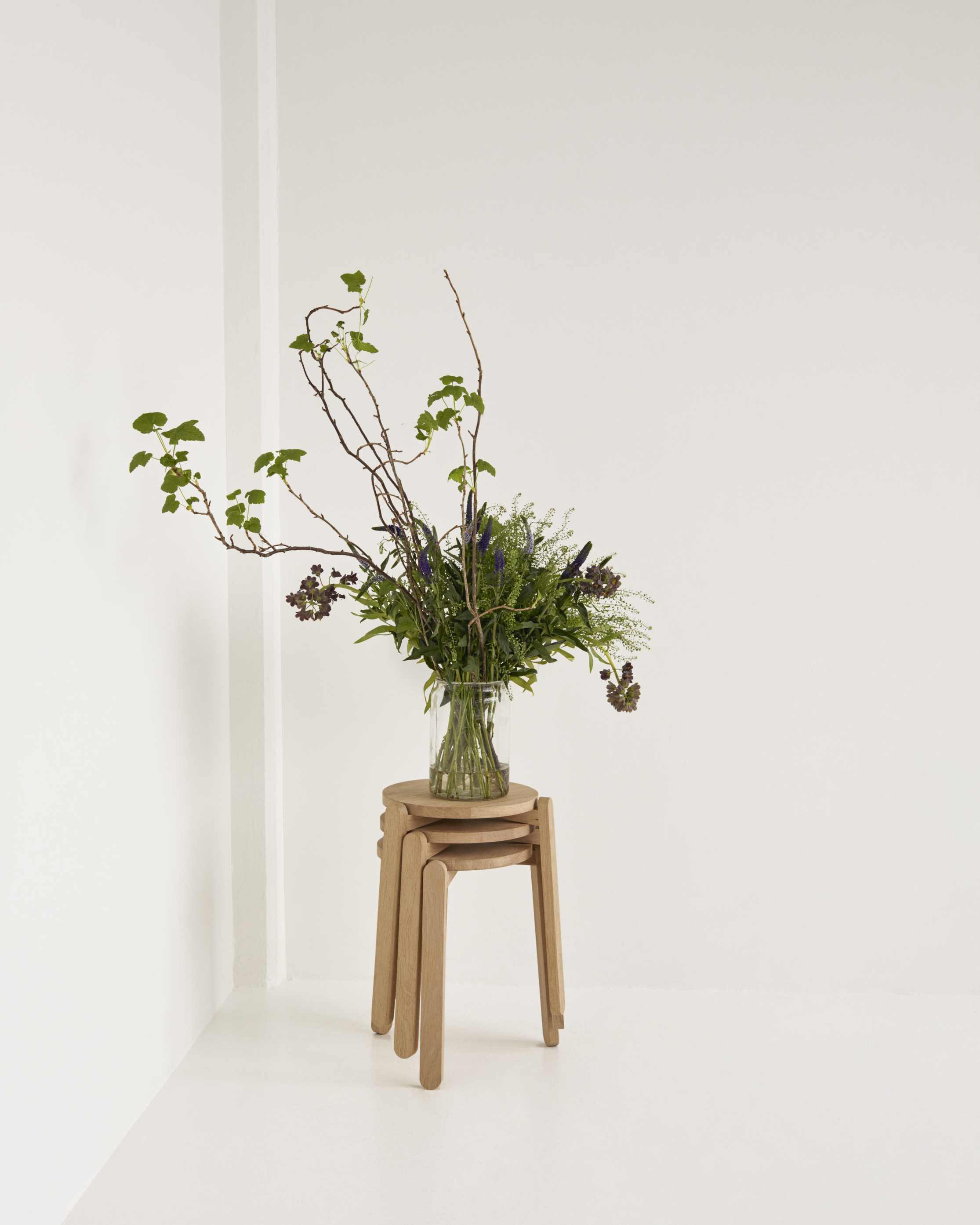 Drei Nomad Stool Hocker von Skagerak, gestapelt mit Blumenvase, helle minimalistische Einrichtung.