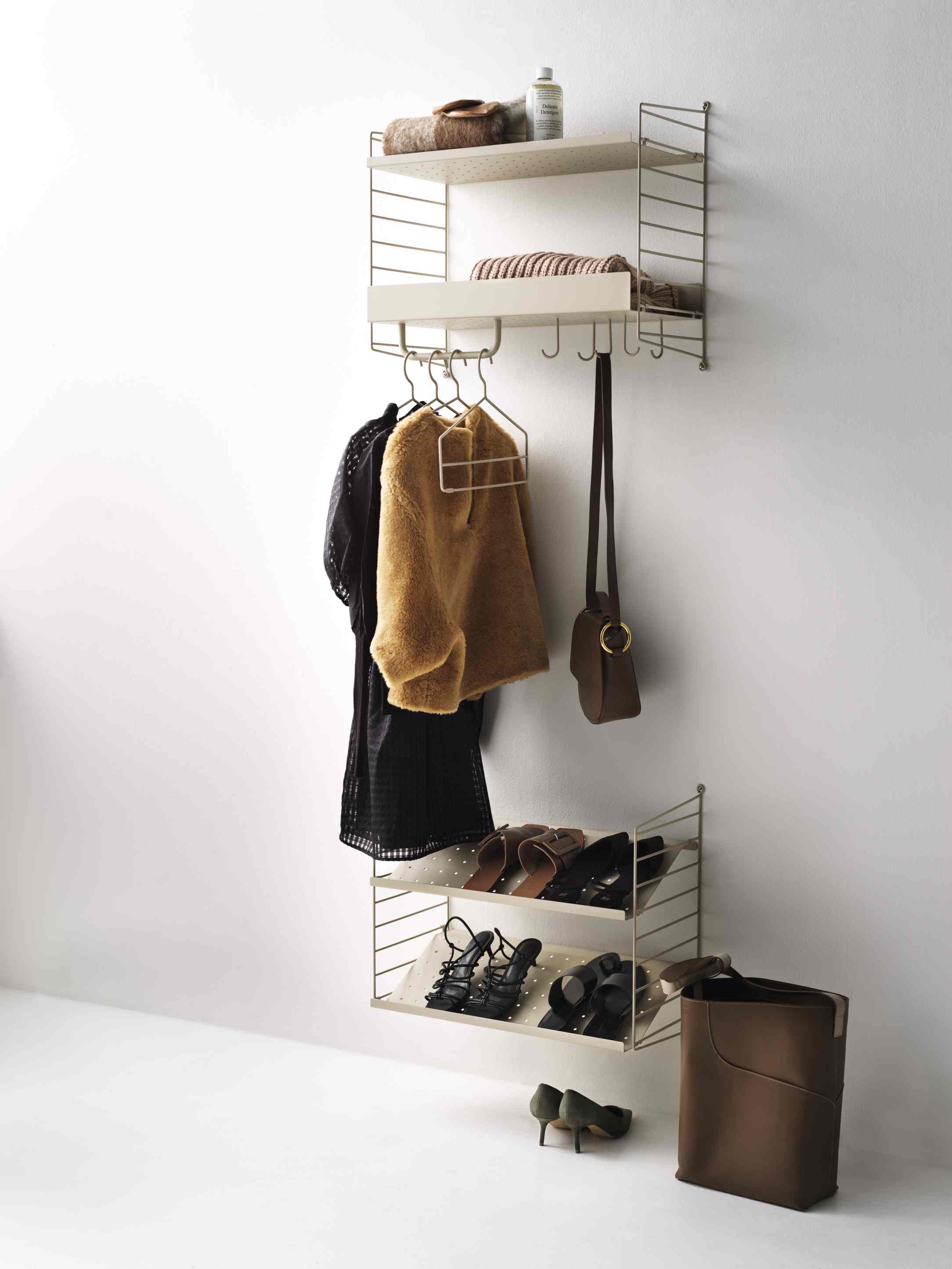 Beiges String Regalsystem an der Wand mit Kleidung, Schuhen und Accessoires für Flur und Garderobe.