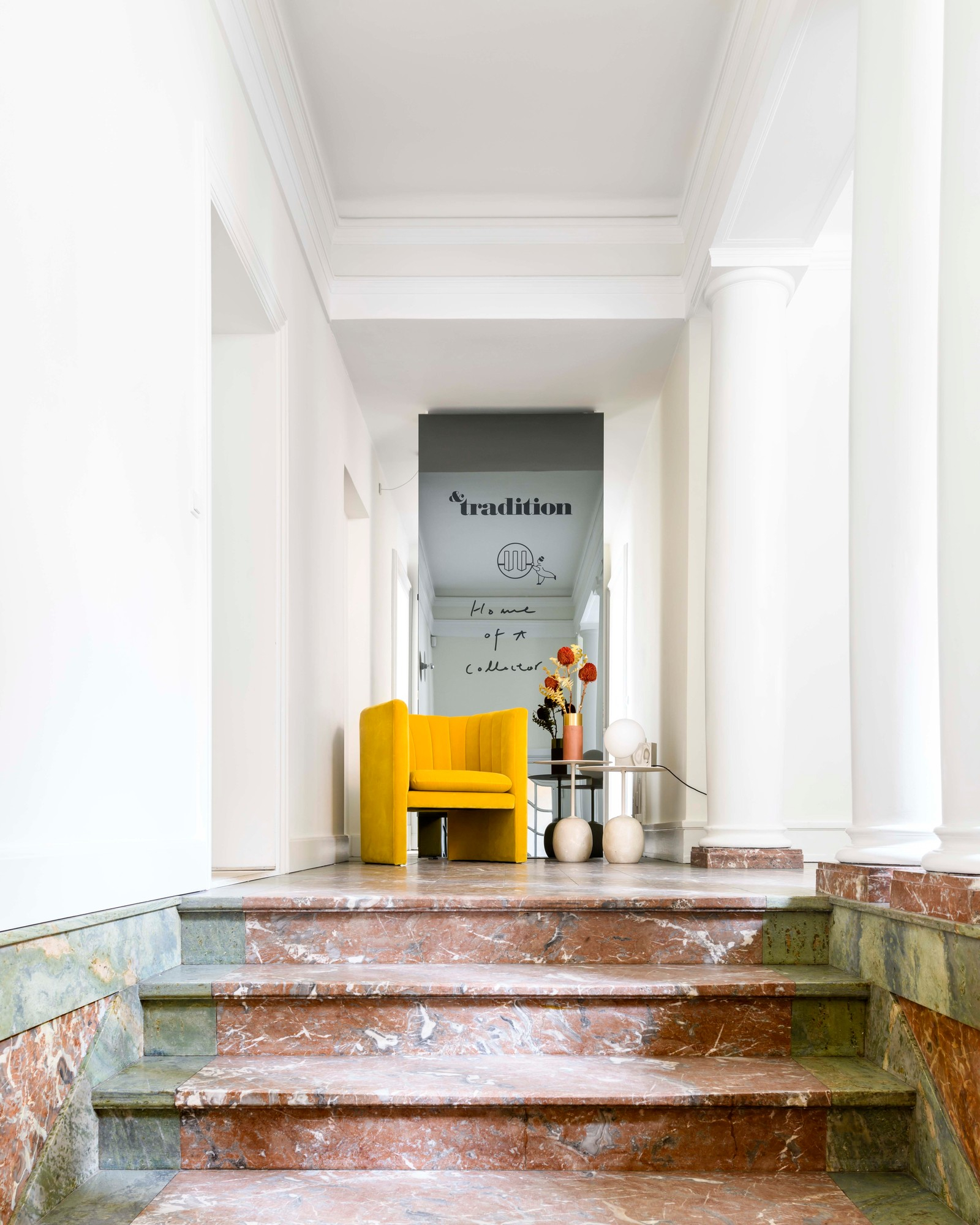 Gelber Loafer Sessel von AndTradition in einem eleganten Interieur mit Marmortreppe und Säulen.