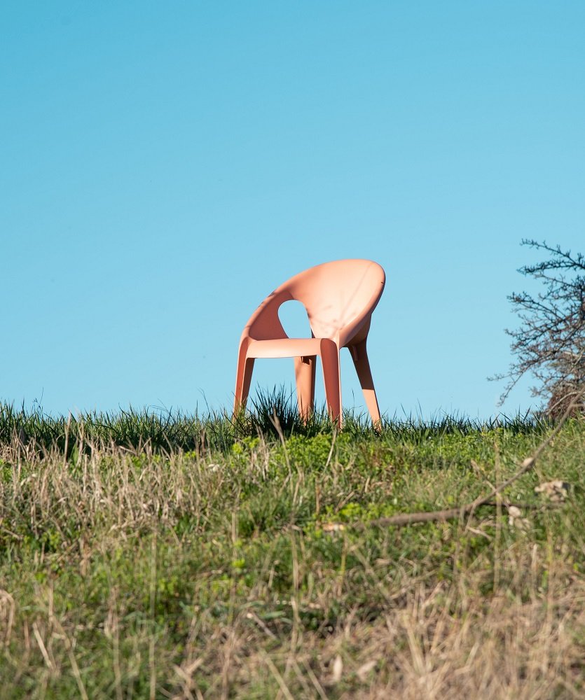 Pfirsichfarbener Bell Chair Outdoor Stuhl von Magis auf einer Wiese vor blauem Himmel. Stapelbarer Design Gartenstuhl.