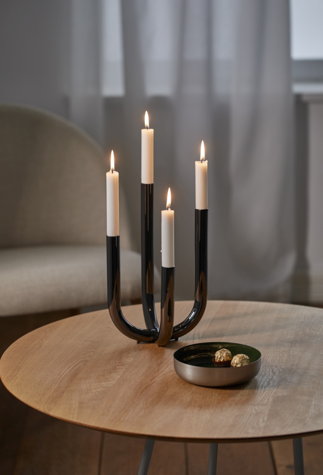 Philippi Festive Leuchter mit vier brennenden, weißen Kerzen auf einem Holztisch. Dekorative Beleuchtung.