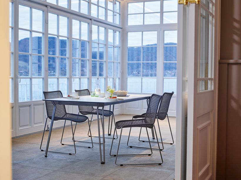 Weishäupl Slope Chair Outdoor Stuhl, graues Metallgestell mit Netzstruktur, im Essbereich mit Seeblick.