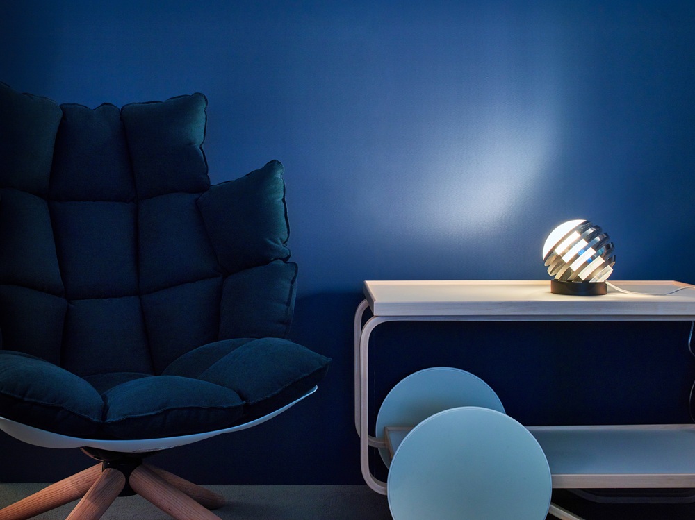 Bulo Tischleuchte Tecnolumen auf Tisch, neben Sessel vor blauer Wand. Design Lampe.