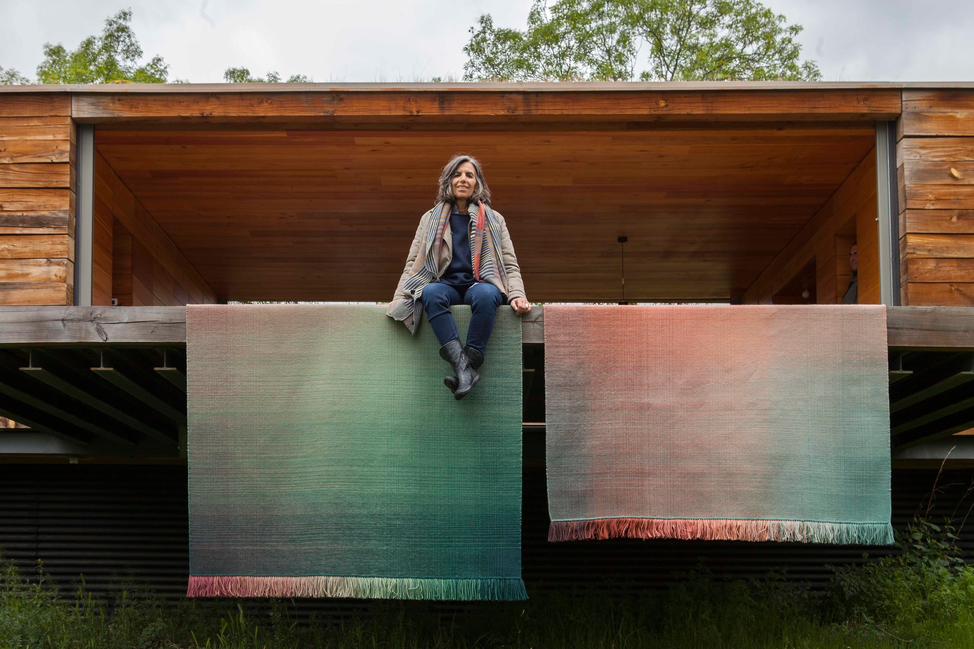 Frau sitzt auf Balken vor zwei Nanimarquina Shade Teppichen mit Farbverlauf und Fransen.