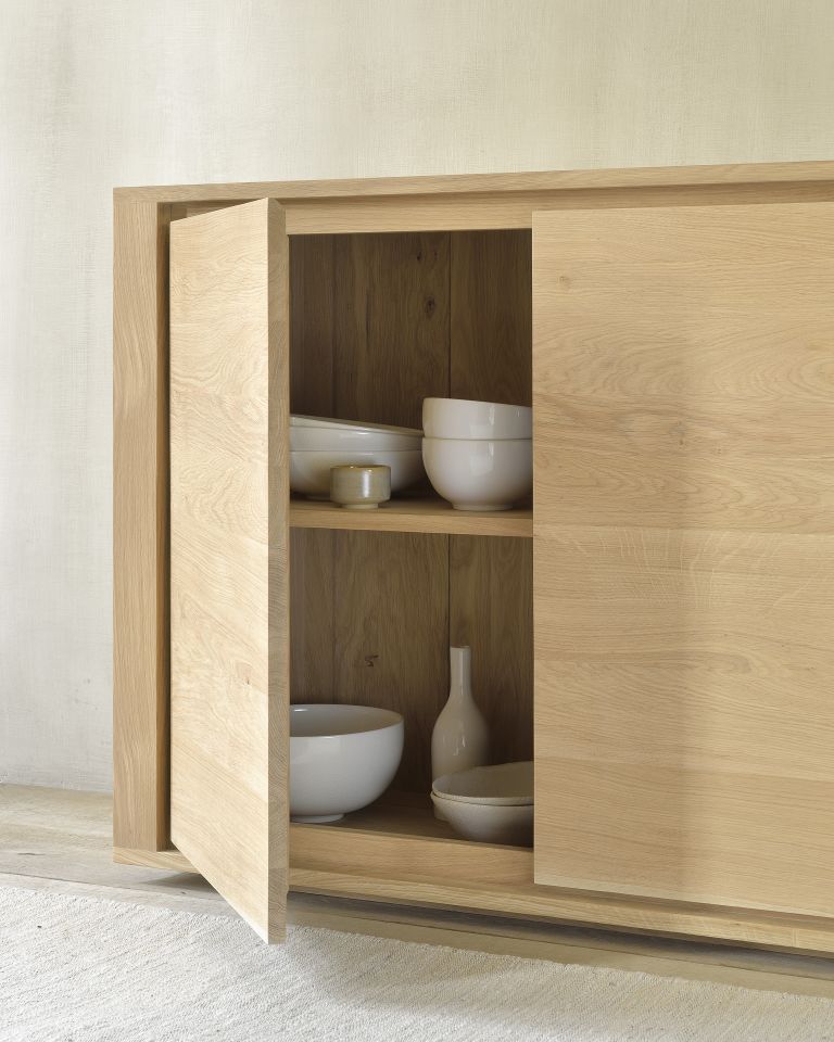 Detailaufnahme: Ethnicraft Sideboard aus Eiche mit offener Tür und Geschirr. Massivholz Möbel.
