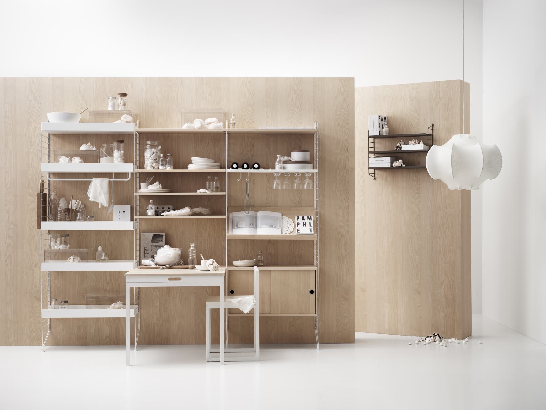 Helles Wohnzimmer mit String Furniture Regalsystem, Schreibtisch und Stuhl vor einer Holzvertäfelung.