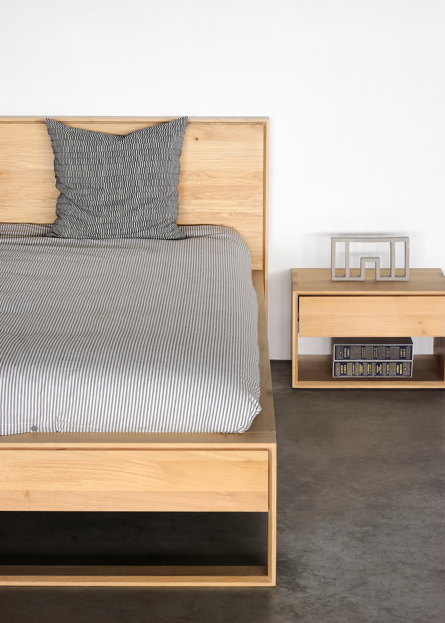 Nordic II Nachttisch aus Eiche von Ethnicraft neben einem Bett mit Schublade und Ablage.