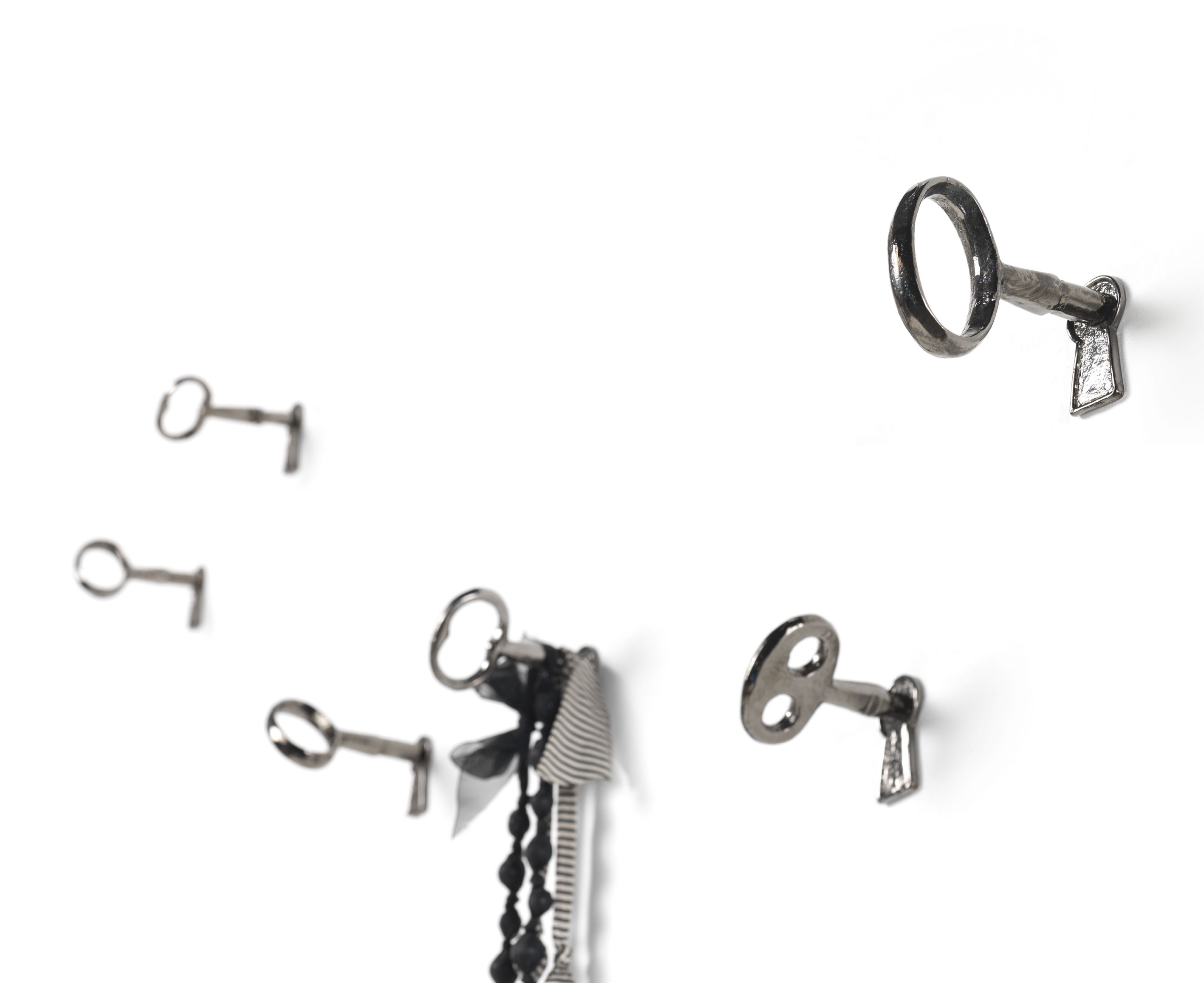 Mogg Memorie Wandhaken 4er Set: Schlüssel-förmige Wandhaken aus Metall an einer weißen Wand.