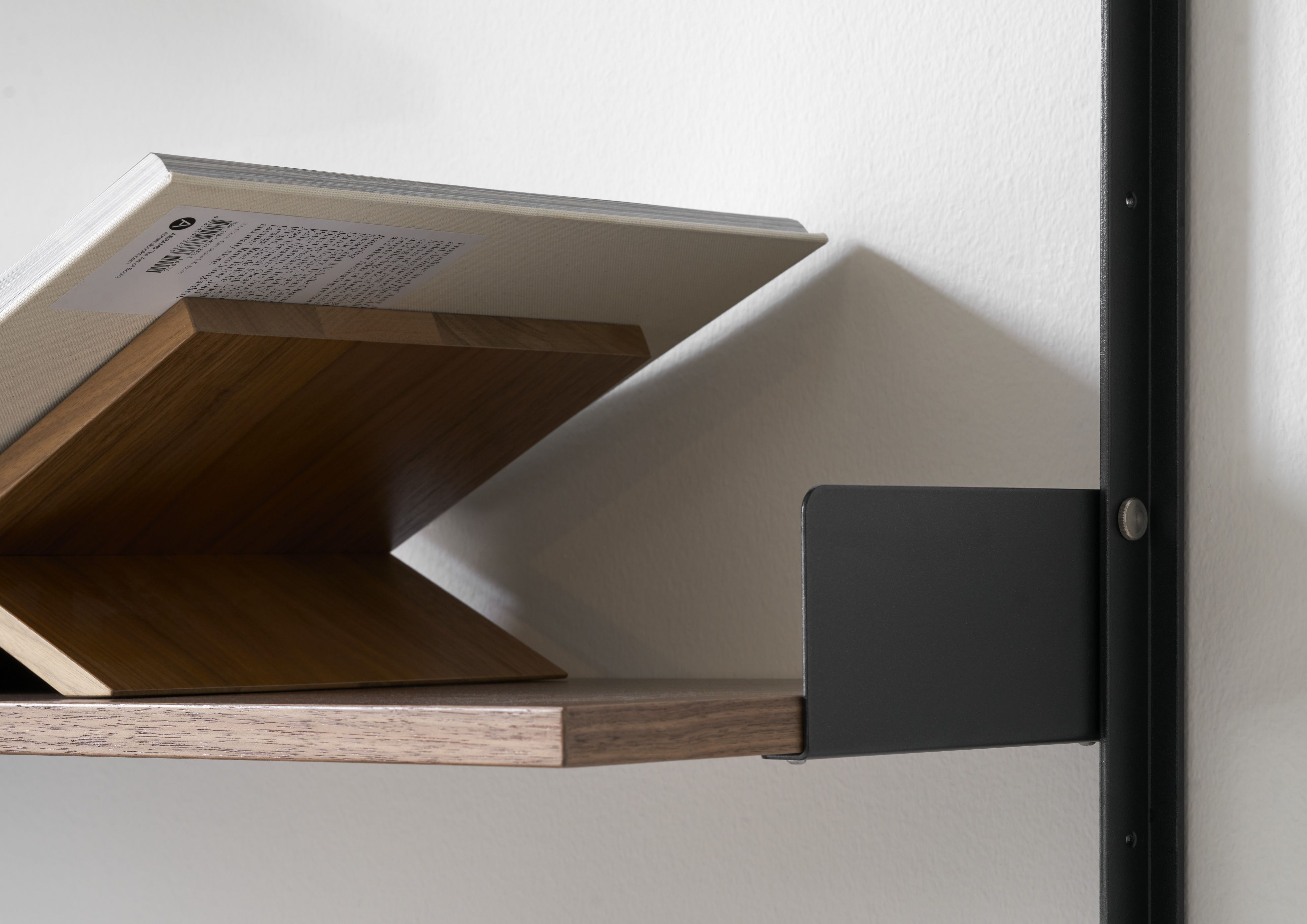 Detailaufnahme eines New Works Wandregals 1900 in Walnuss mit Buchstütze und Buch.