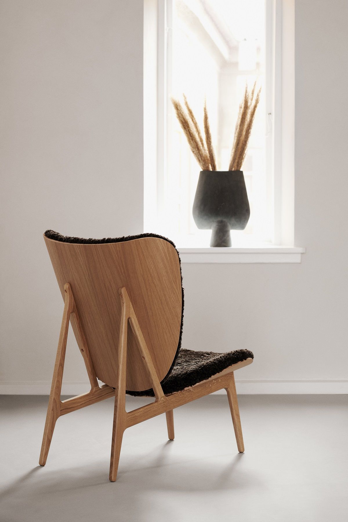 Rückansicht des Elephant Lounge Chair Sessels von NORR11 mit Holzrahmen und schwarzem Schaffellbezug.