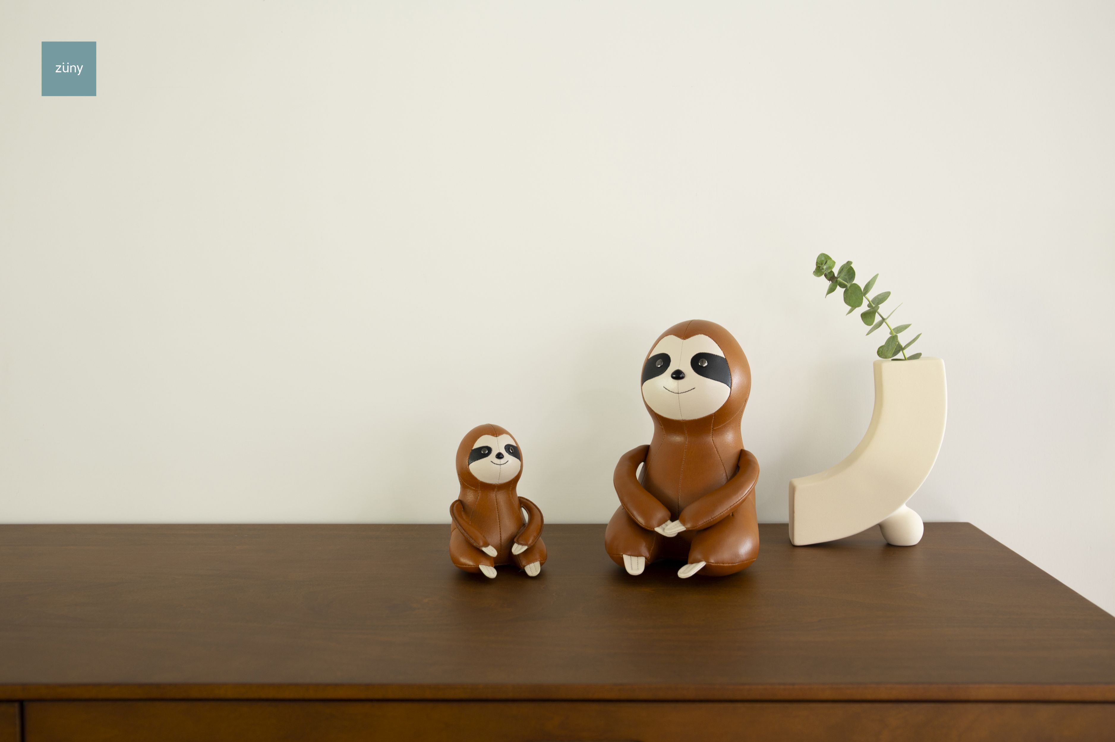 Zwei Züny Faultier Briefbeschwerer in Tan und Weizen auf einem Holzschrank.