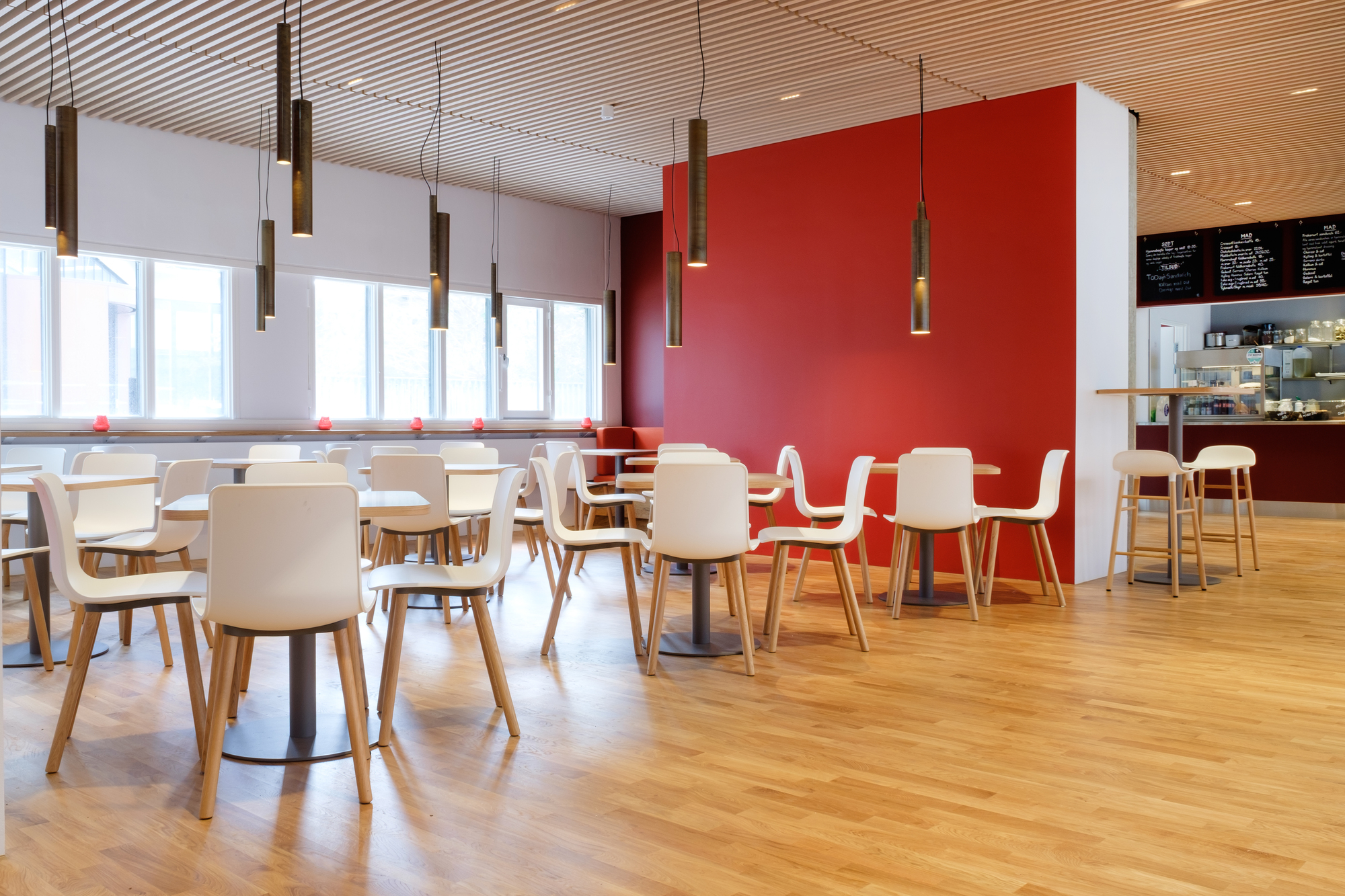 Innenaufnahme mit vielen weißen Hal Ply Wood Stühlen von Vitra an Tischen in einem Restaurant.