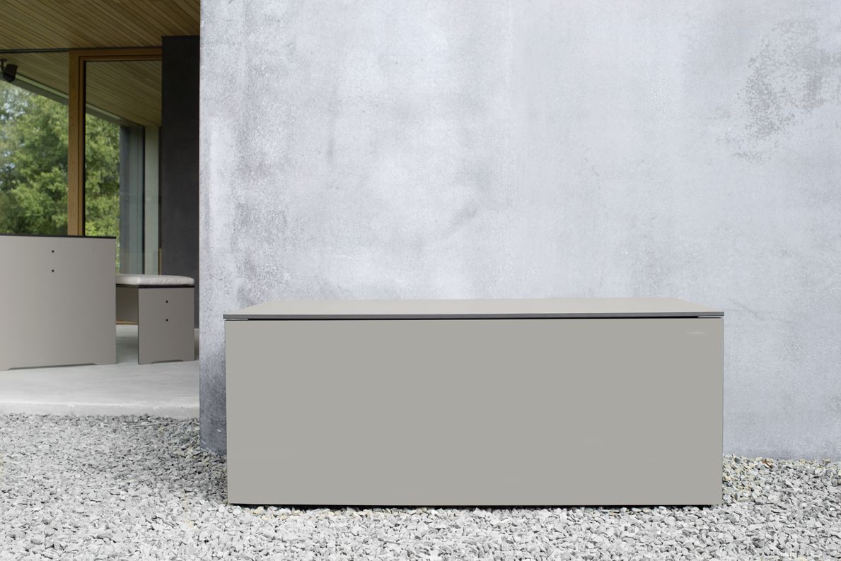 Anthrazitfarbene EL Pecho Kissentruhe von Conmoto auf Kiesboden vor einer Betonwand. Stauraum für Gartenmöbel.