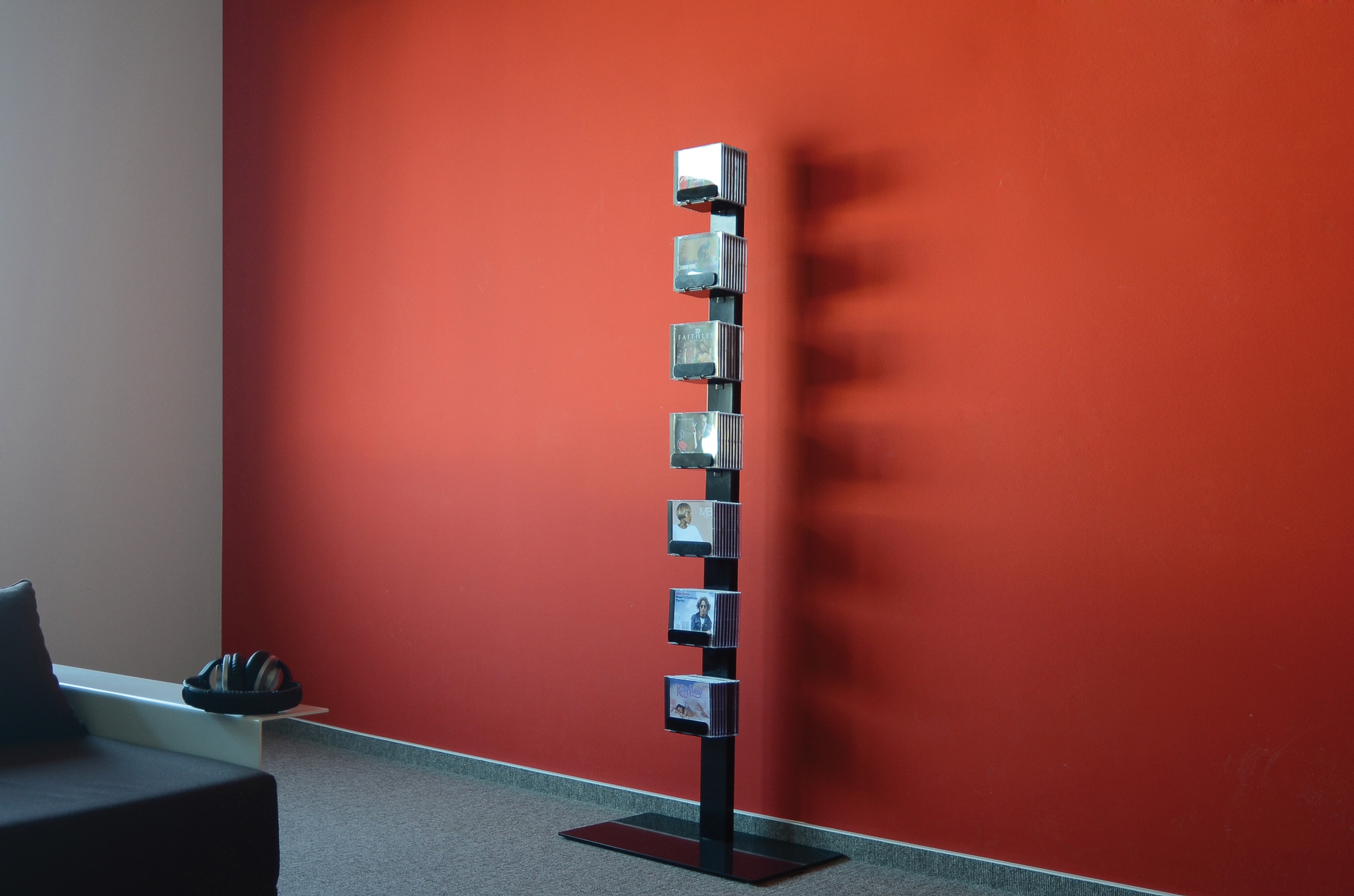 Schwarzes CD-Regal "CD-Baum" als Einzel-Standregal vor roter Wand, gefüllt mit CDs. Möbel zur CD-Aufbewahrung.